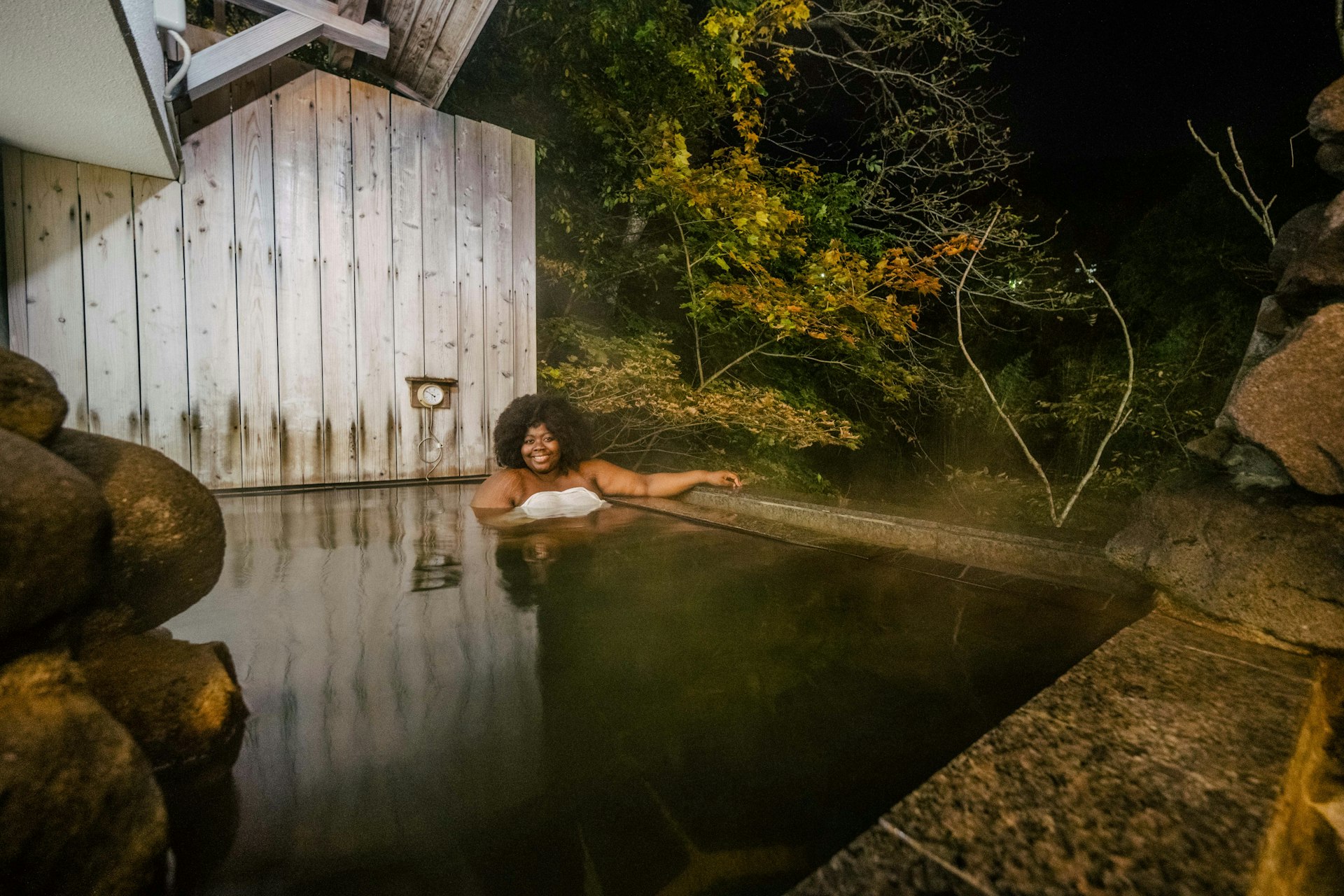 A woman relaxes in an onsen surrounded by nature