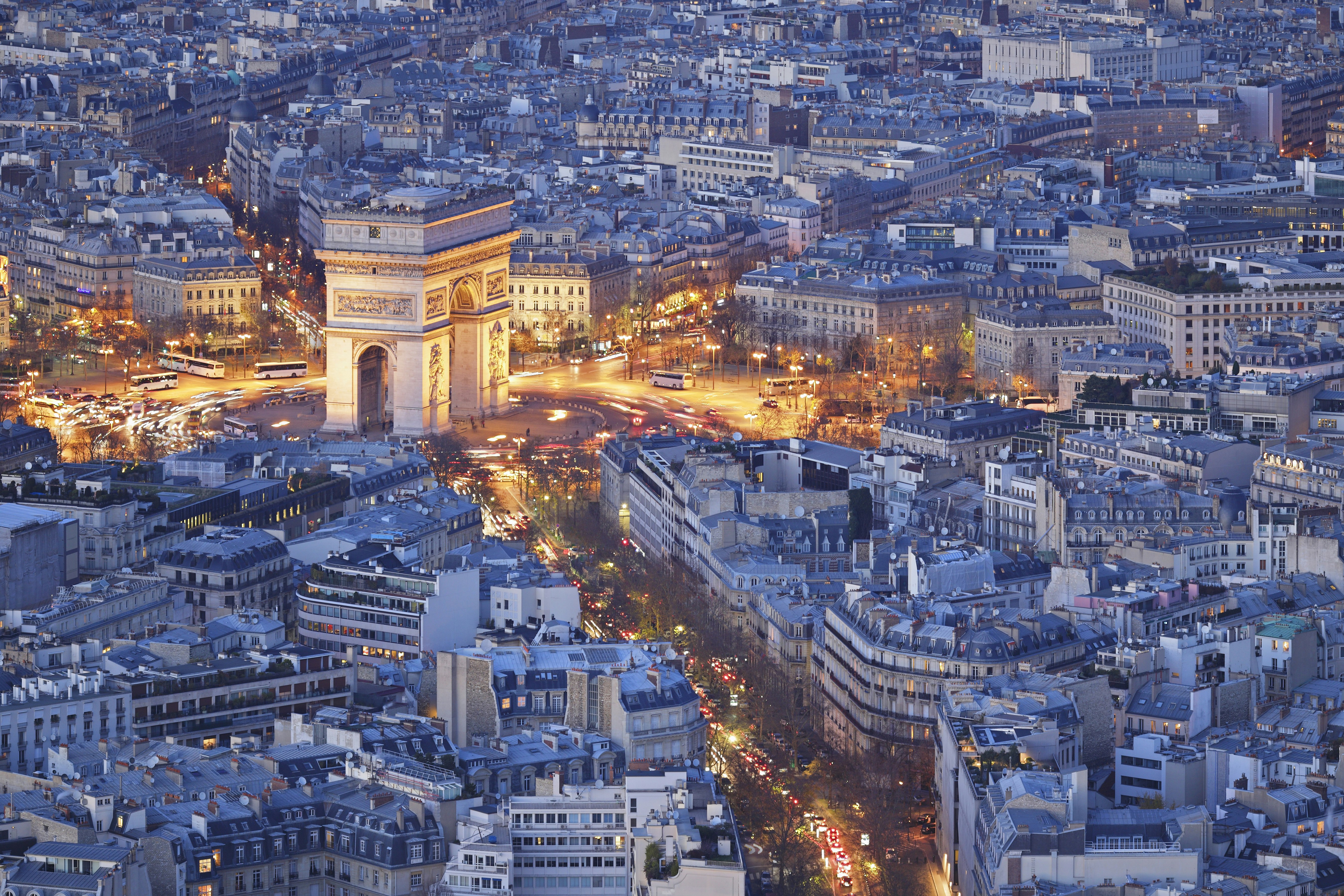 The Arc de Triomphe is lit up at night in an aerial photo. 