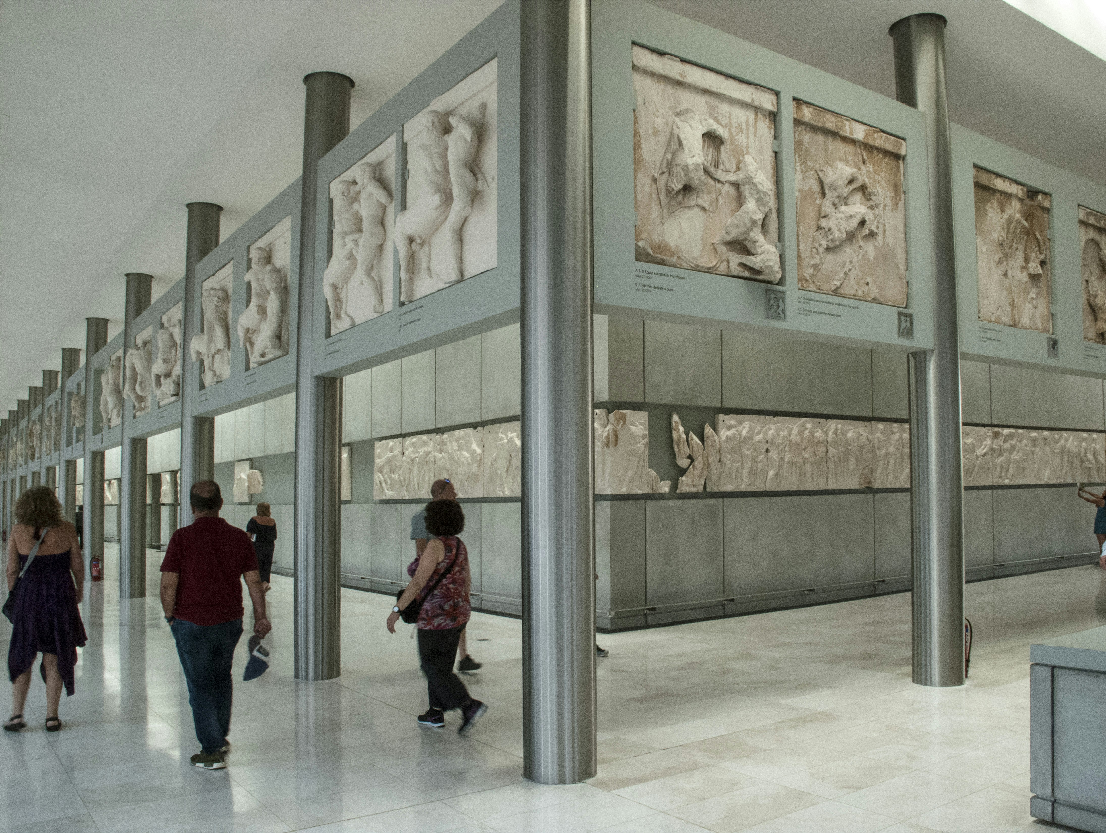 Tourists stroll around the perpendicular walls of the Acropolis Museum lined with some of the remaining friezes which were not removed by Elgin