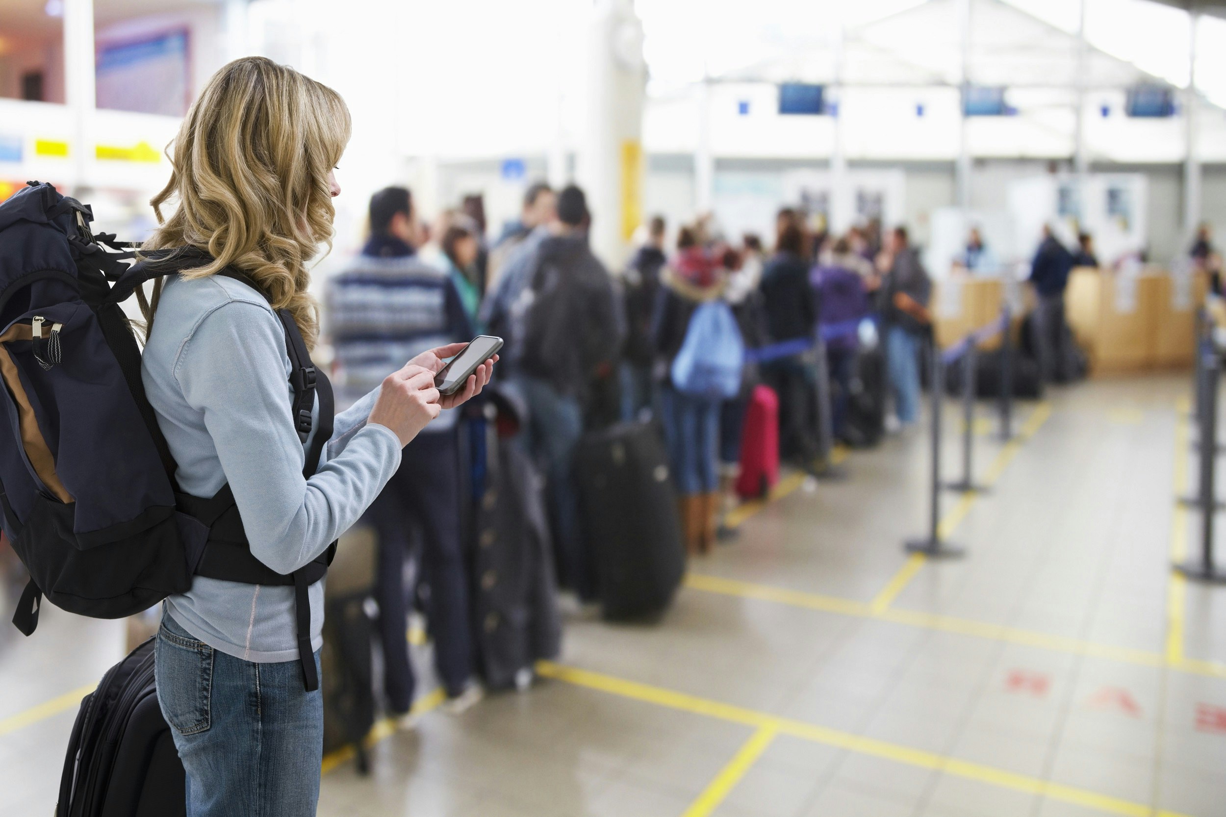 A woman wearing a backpack looks at her phone while she waits in a queue to board a plane