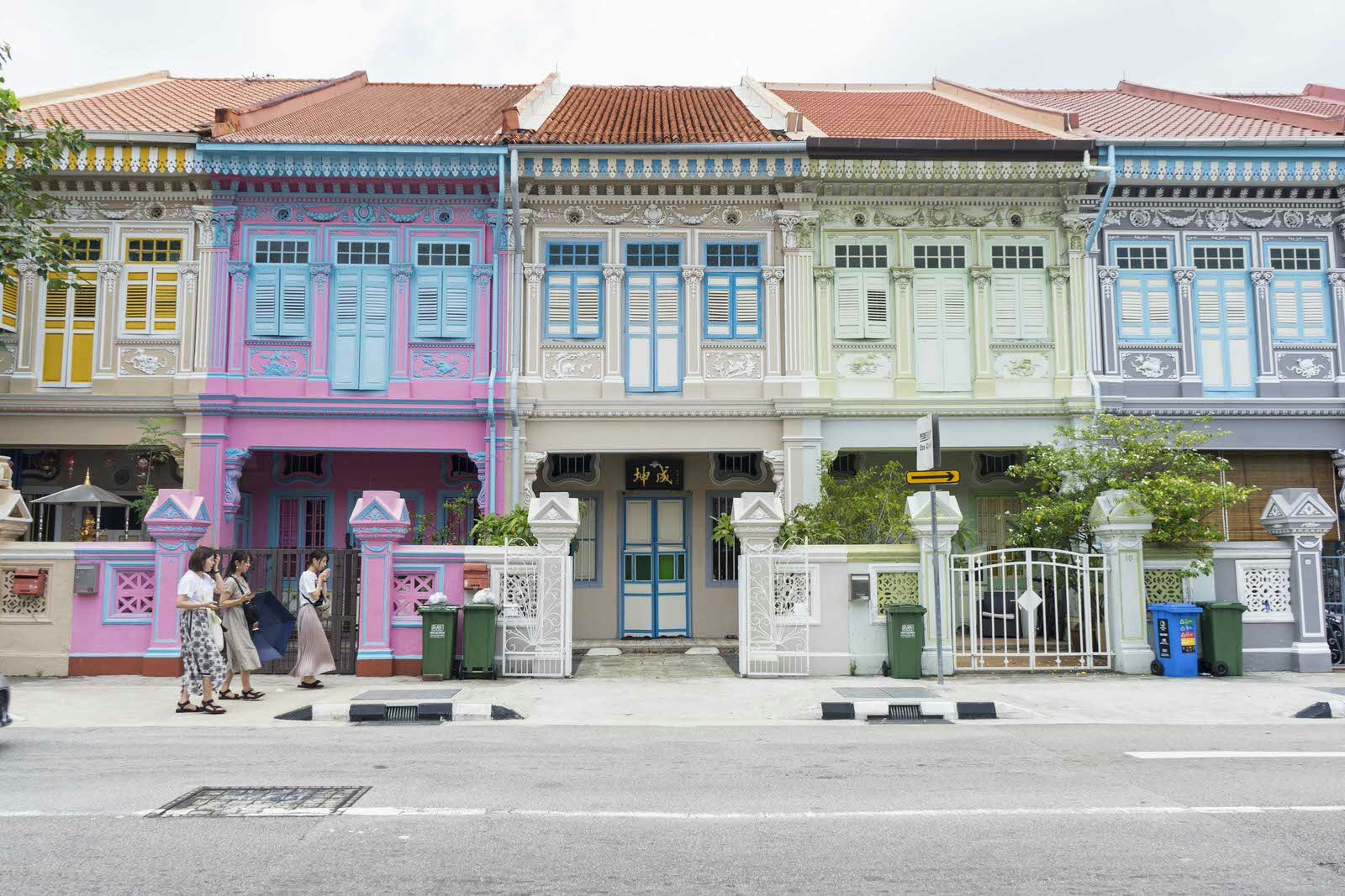 Färgglada Peranakan-hus i Singapore.  Det går tre kvinnor förbi de pastellfärgade hemmen. 