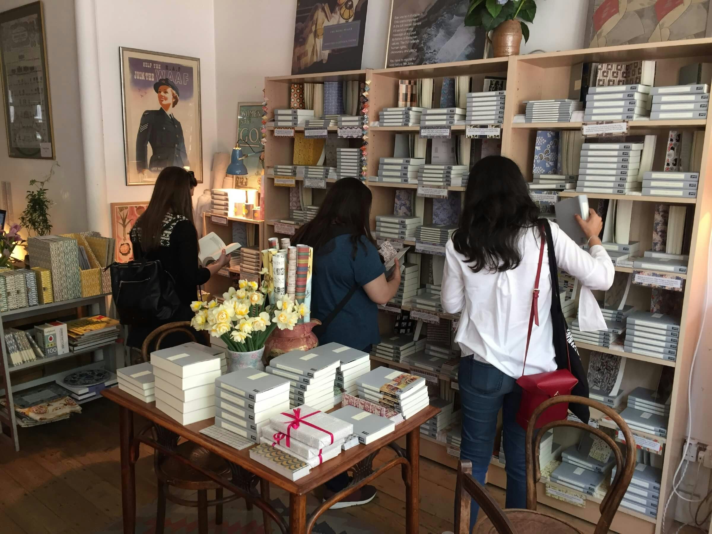 The interior of Persephone Books. Three women browse the book shelves filled with stacks of grey books.
