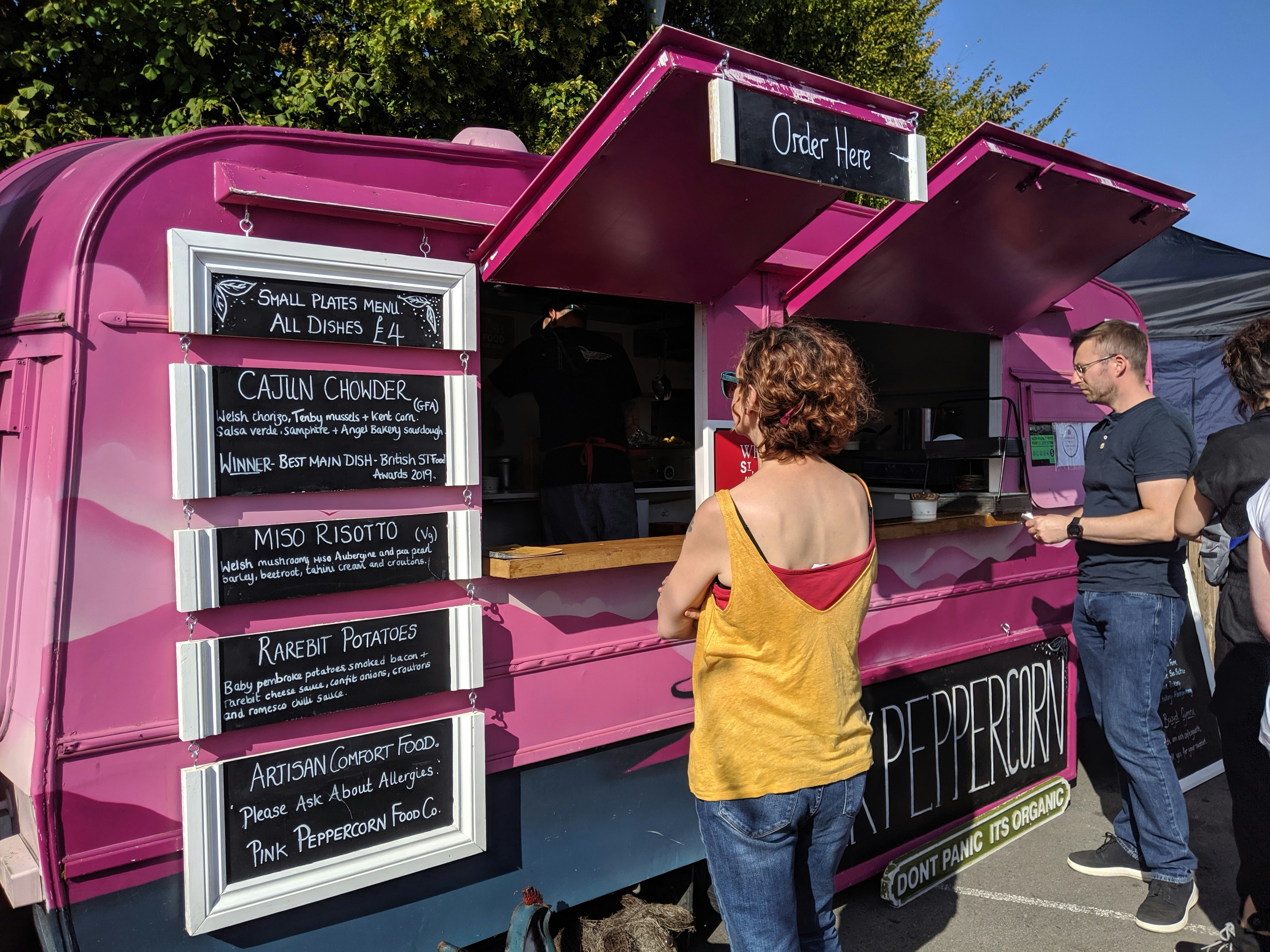 En ljust rosa food truck med en meny som visas på en svart tavla.