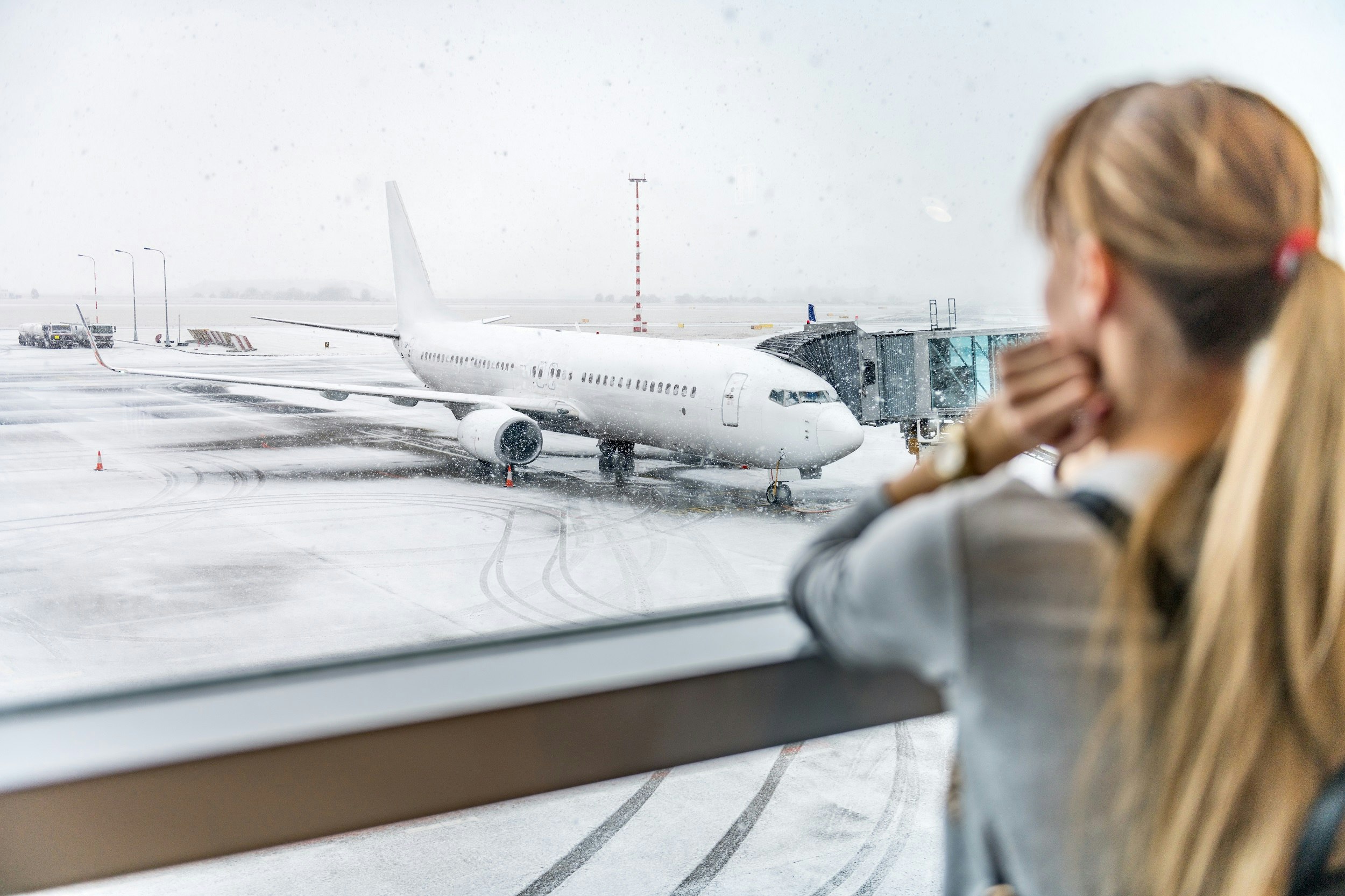 A woman gazes out of the window at a plane waiting at a stand in the snow