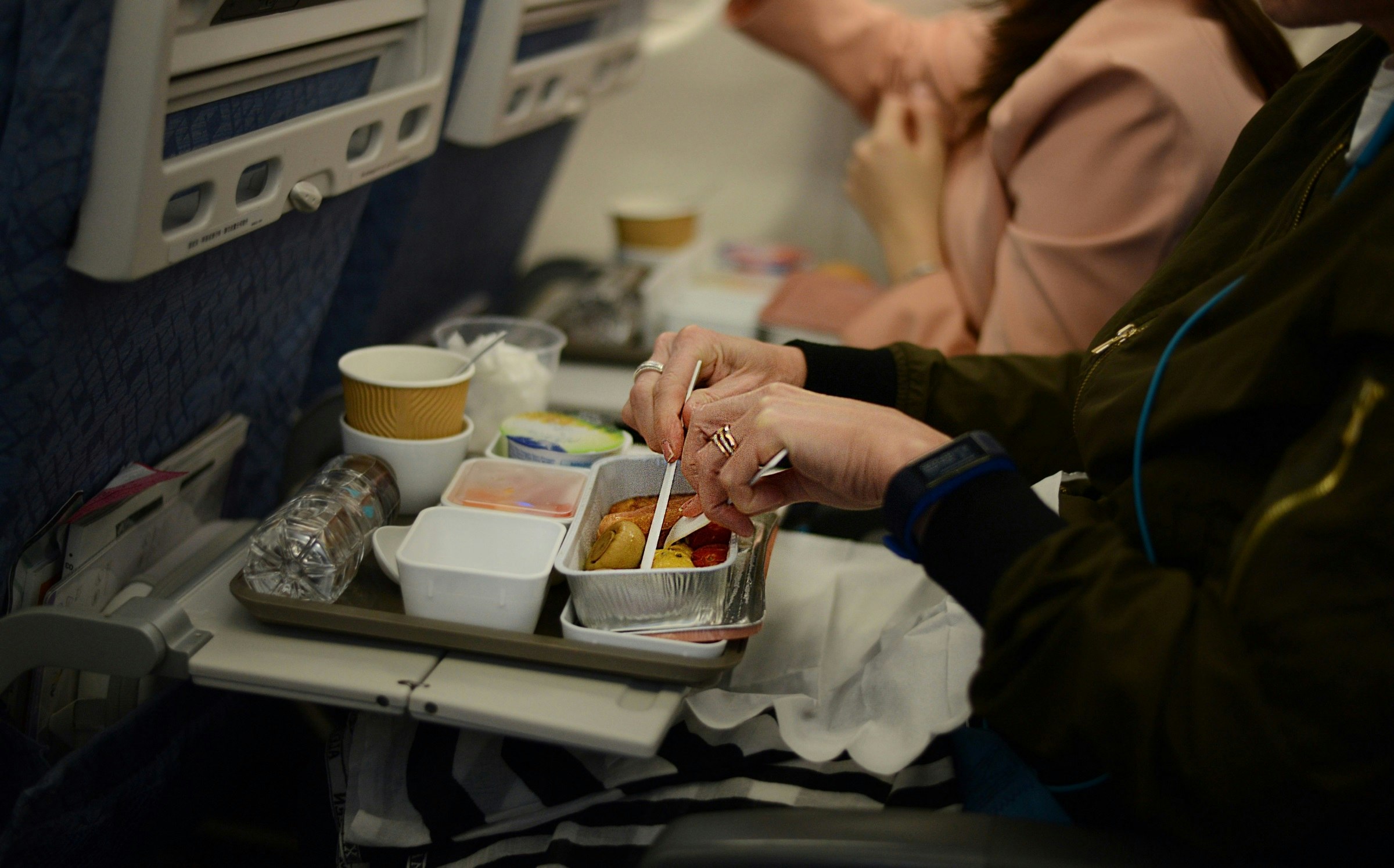 A passenger in economy class starts eating their plane food. The tray is full of plastic containers