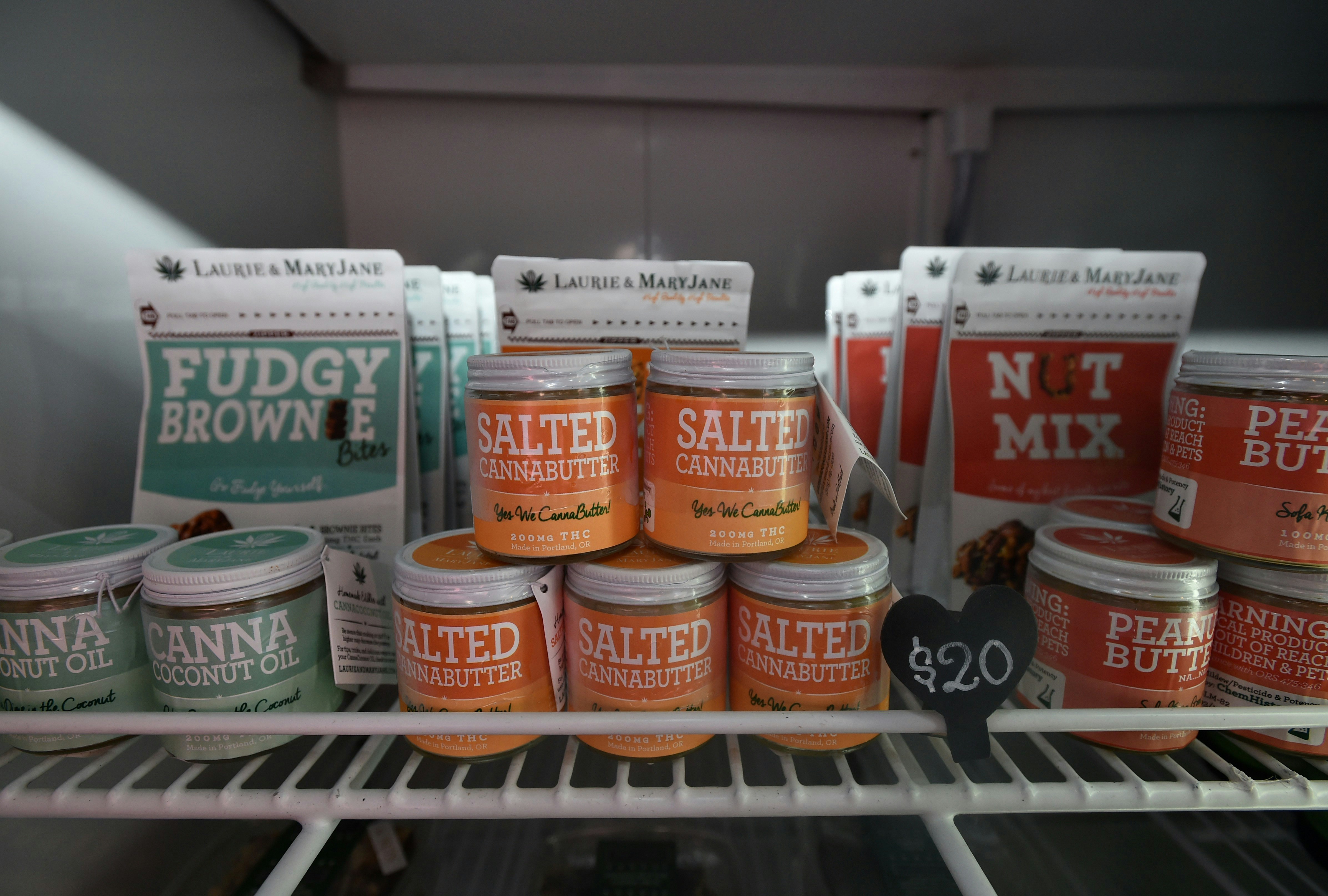 Three rows of edible cannabis products are arranged on a white wire shelf at a Portland, Oregon cannabis dispensary. They include salted cannabutter, fudgy brownies, and an infused nut mix