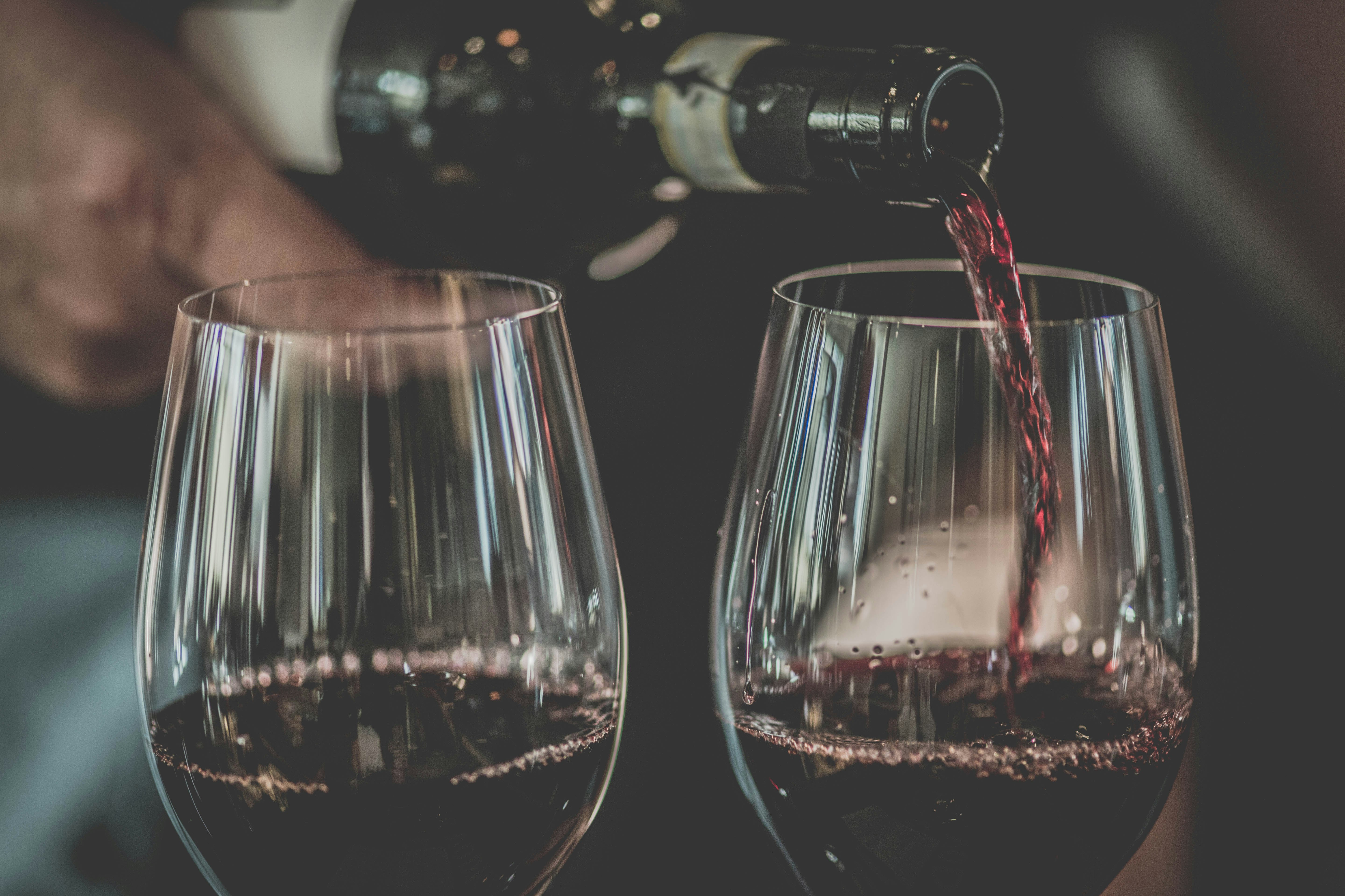 A bottle of red wine being poured into two empty wine glasses