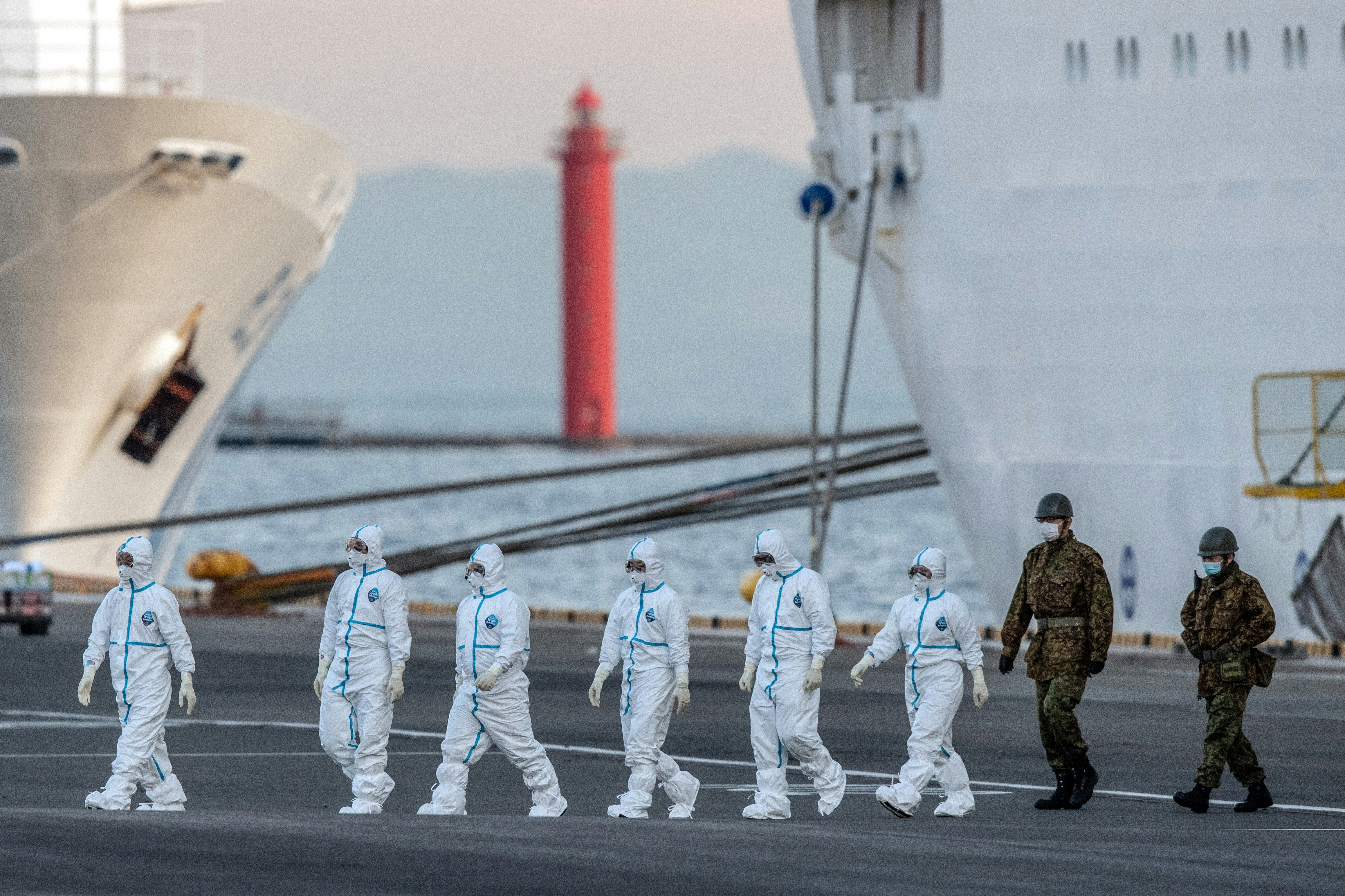 People in protective suits walk away from a cruise ship.