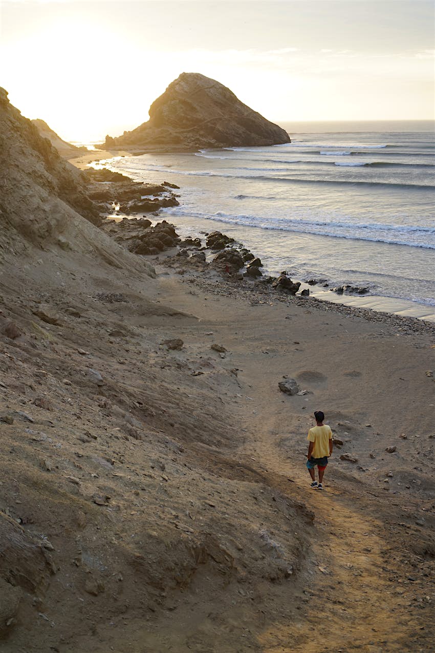 A man walks down a rocky path to a beach