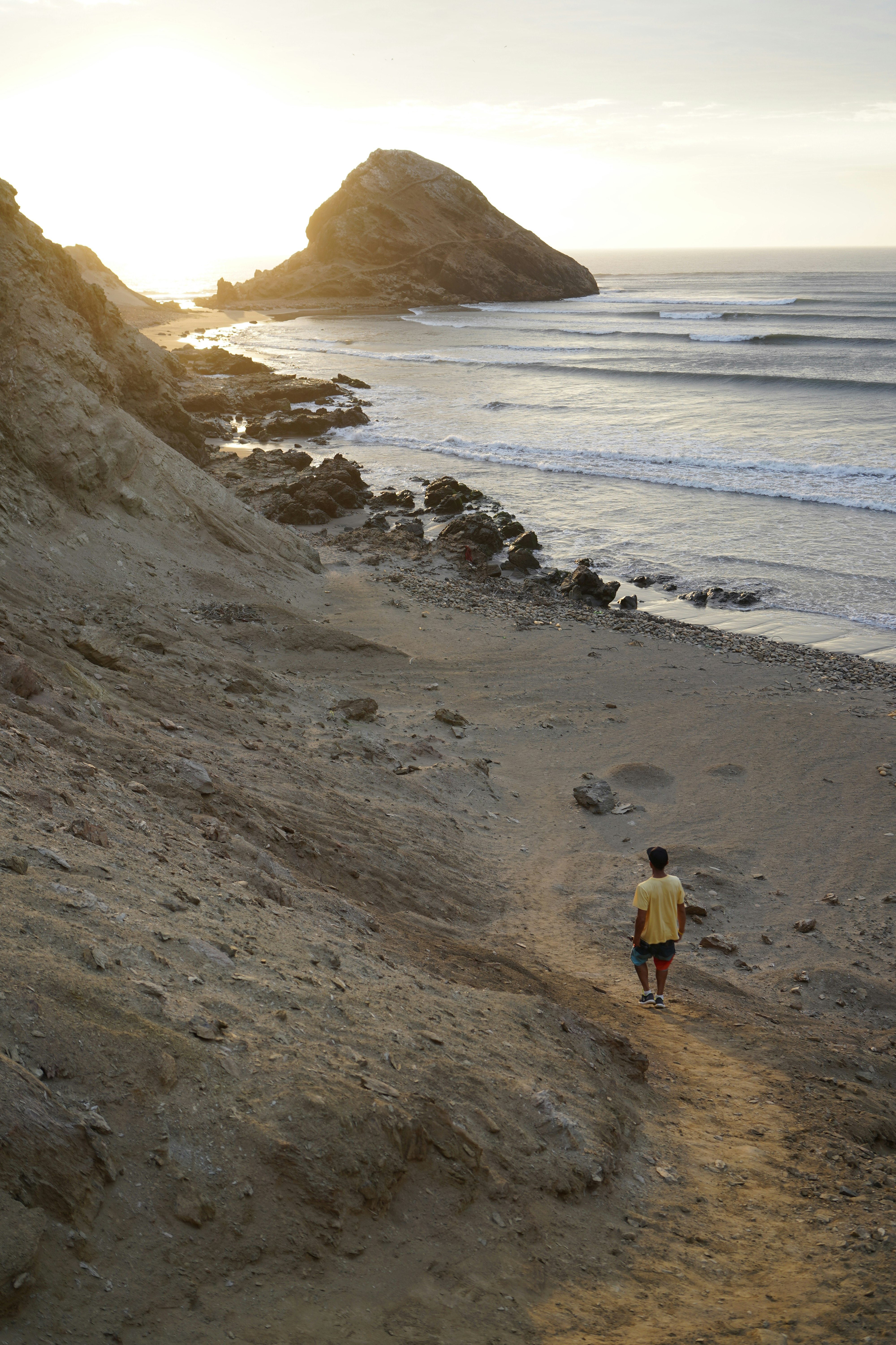 A man walks down a rocky path to a beach