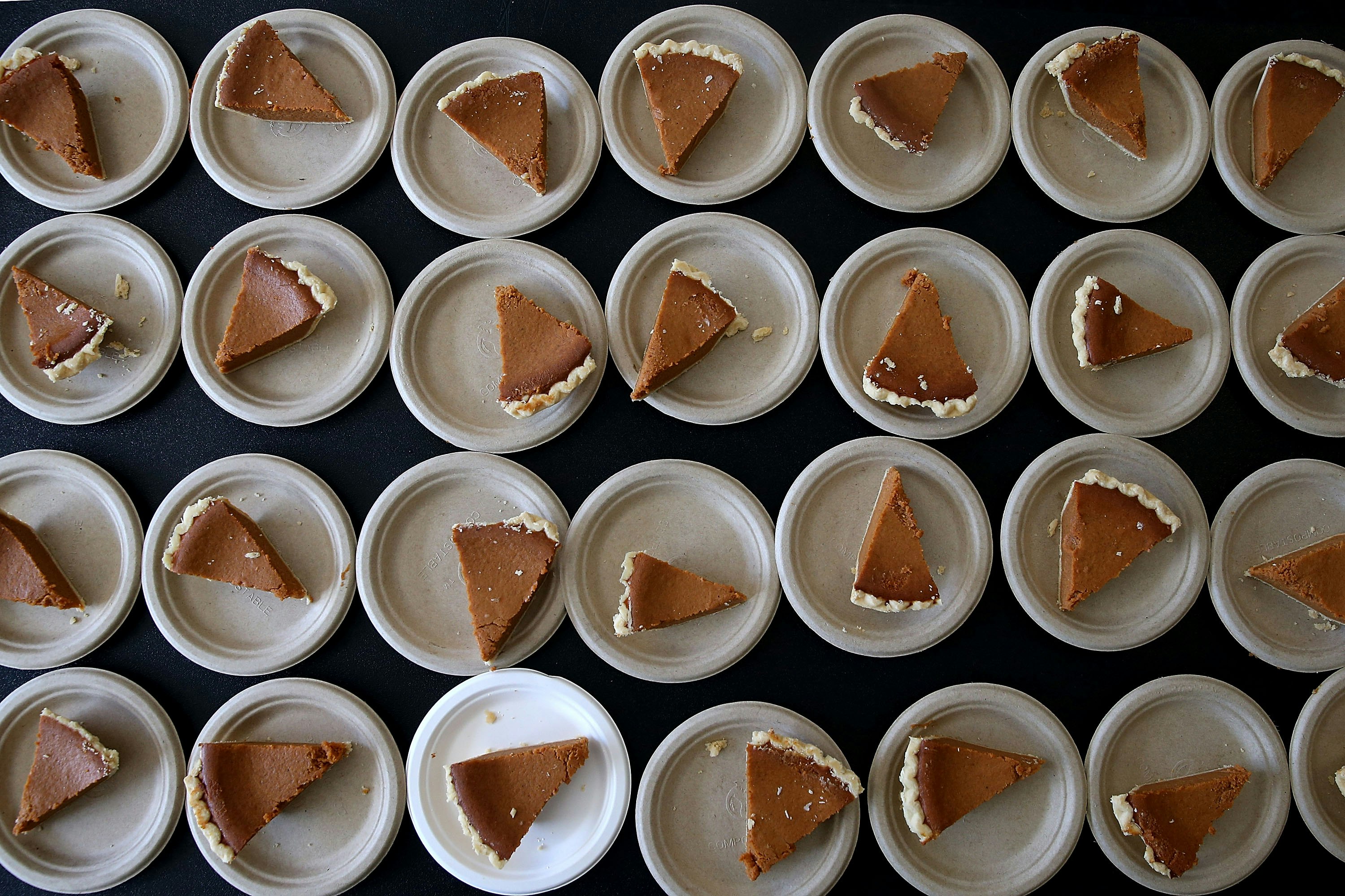 Rows of cardboard plates with slices of pumpkin pie sit on a black table 
