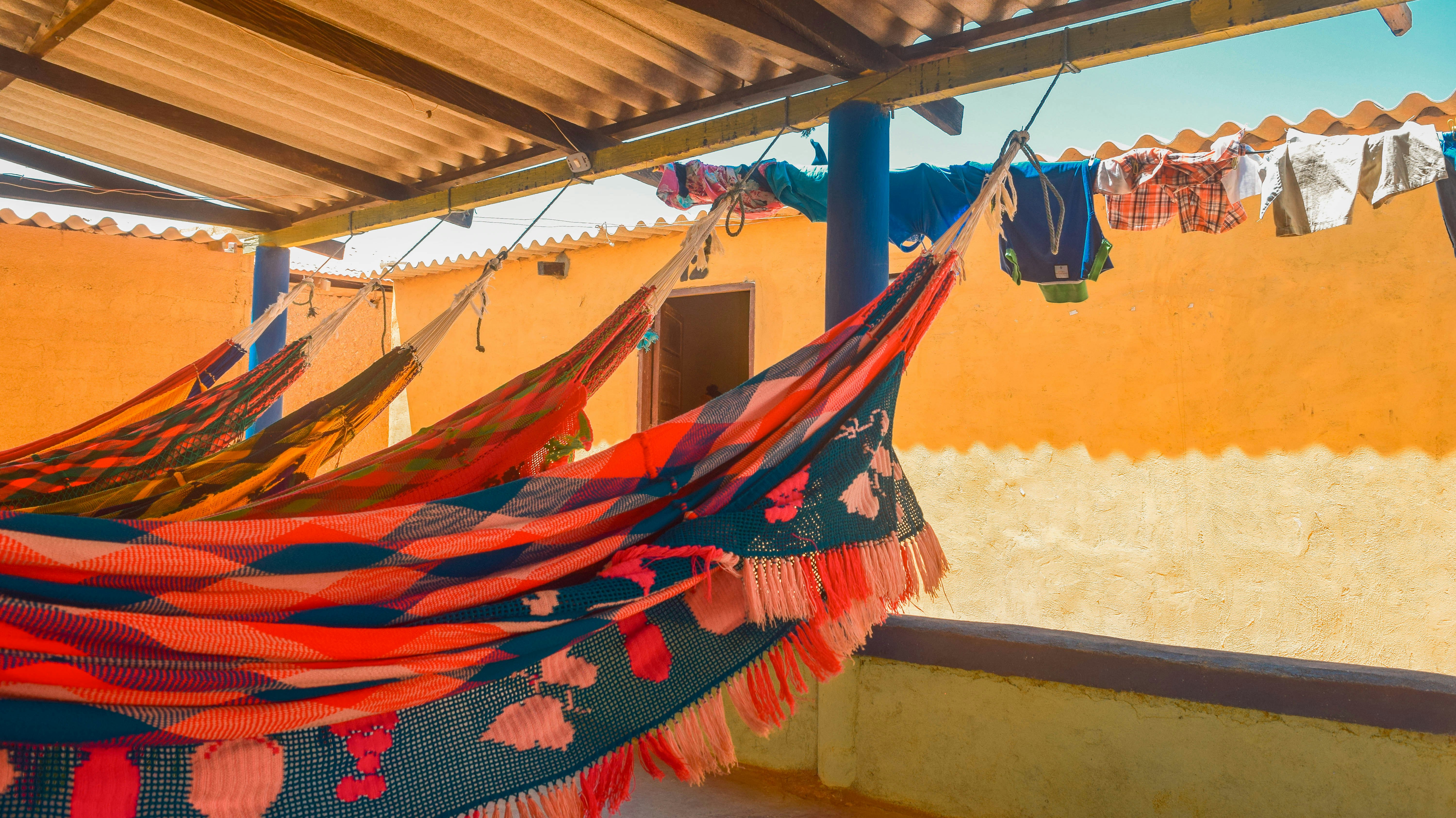 Five bright, patterned hammocks are strung up in a shelter, under a corrugated roof.