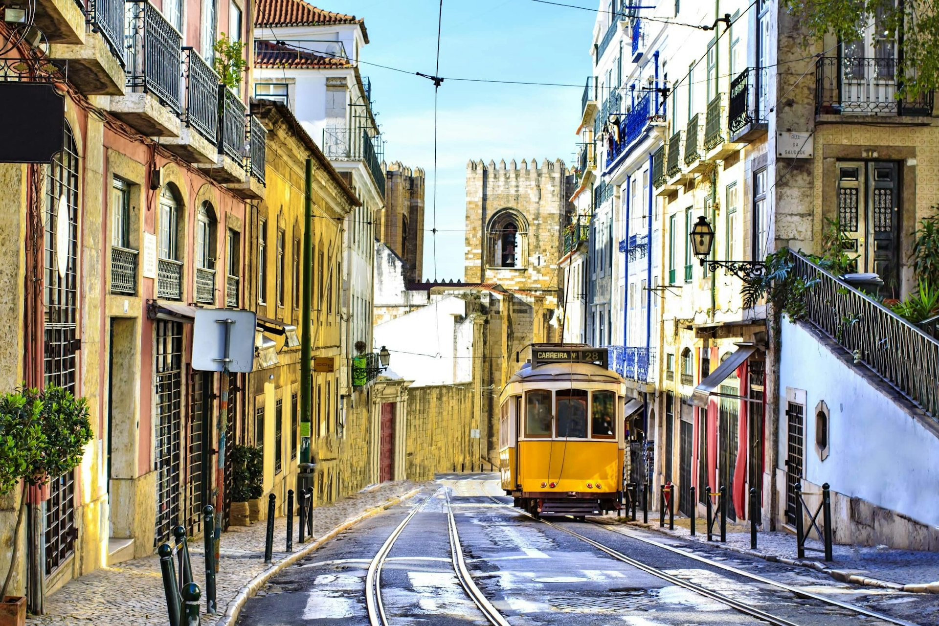 Empty Lisbon street with yellow tram and the bell tower of Lisbon Cathedral in the background.