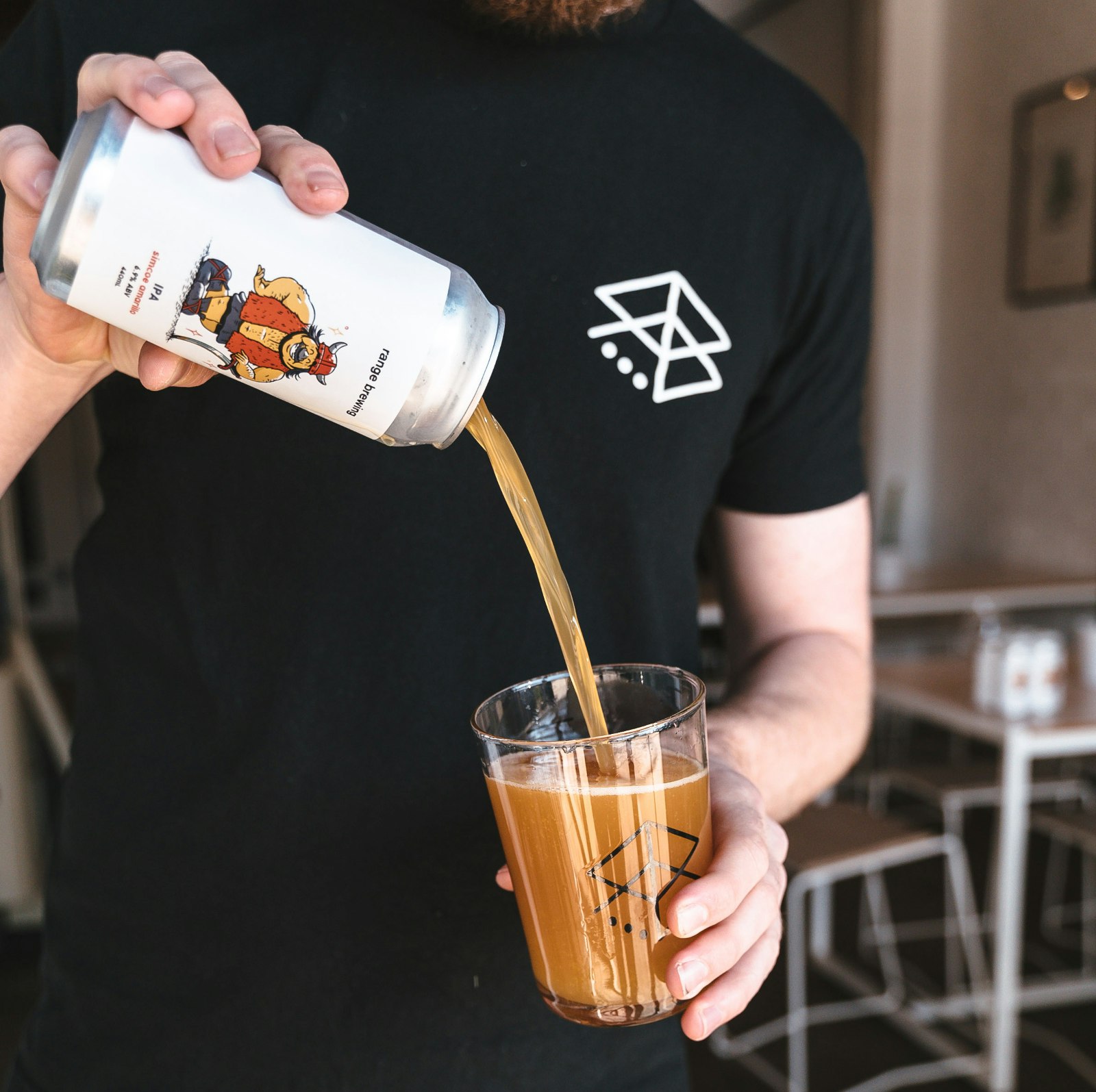 A honey-coloured beer is poured is poured into a pint glass by a man wearing a black Range Brewing t-shirt.