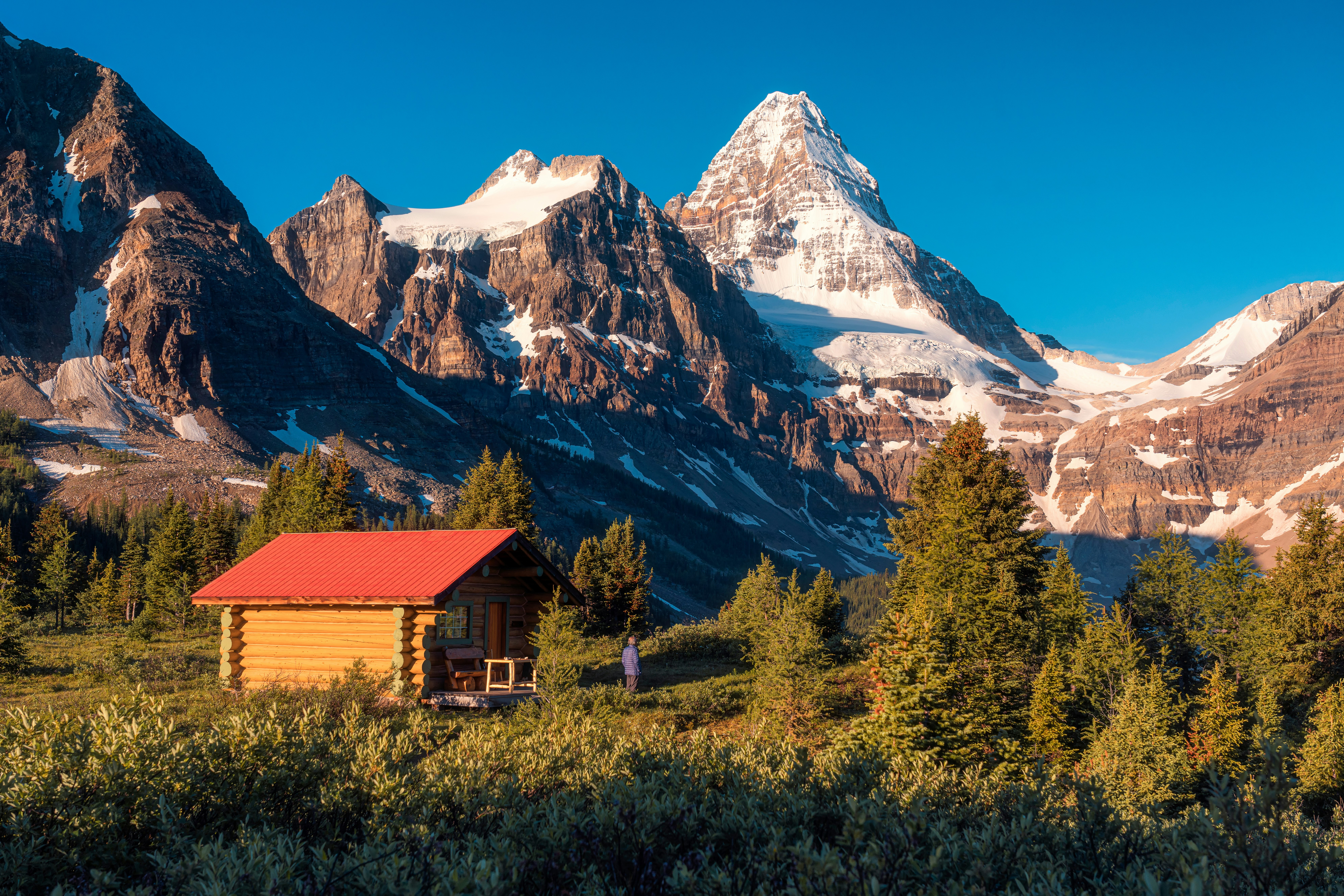 Hiker standing next to a wood cabin and looking at Mt. Assiniboine