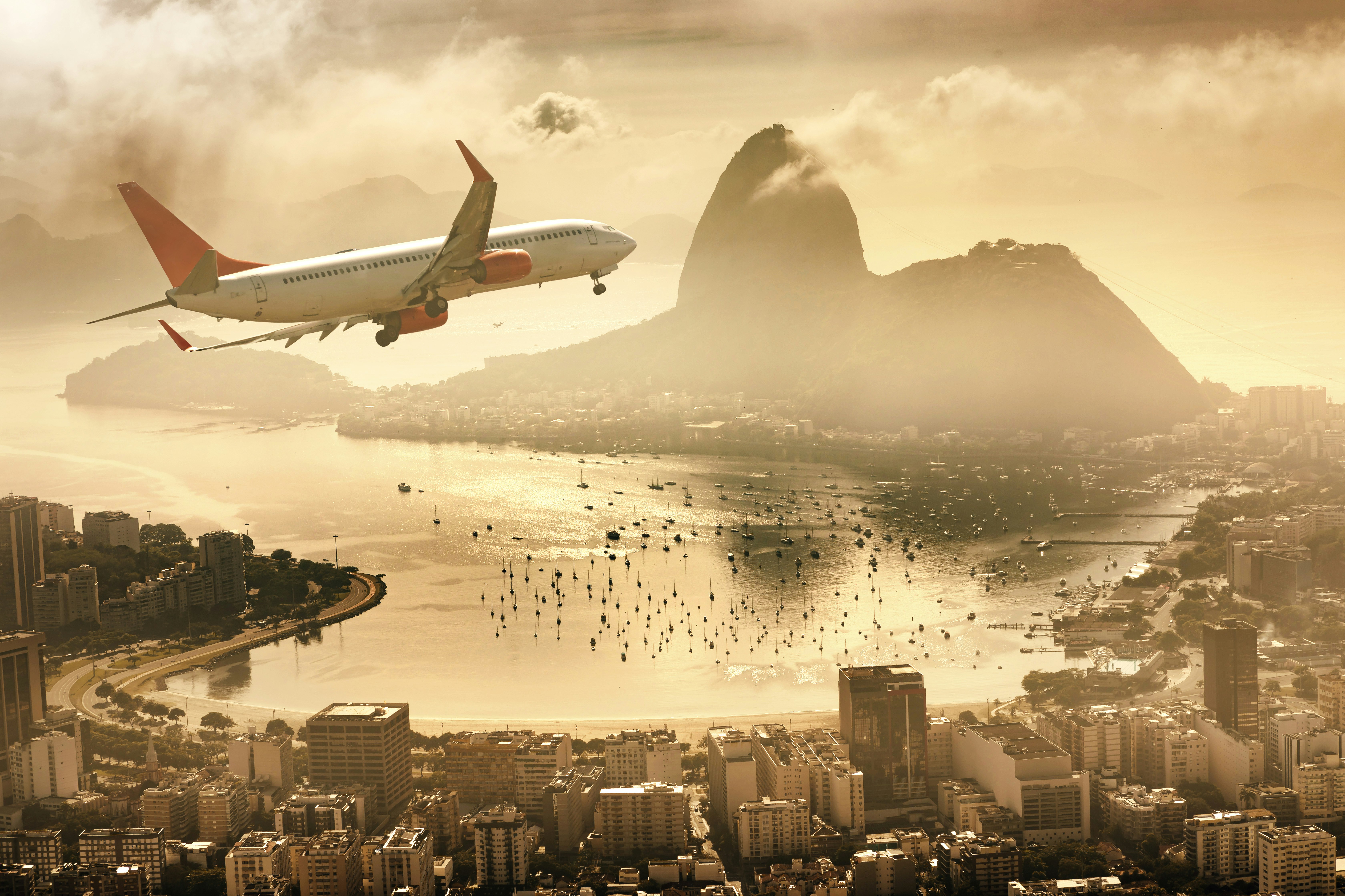 A plane turns towards Rio de Janeiro with the golden hour landscape of Guanabara Bay and Sugarloaf Mountain in the background