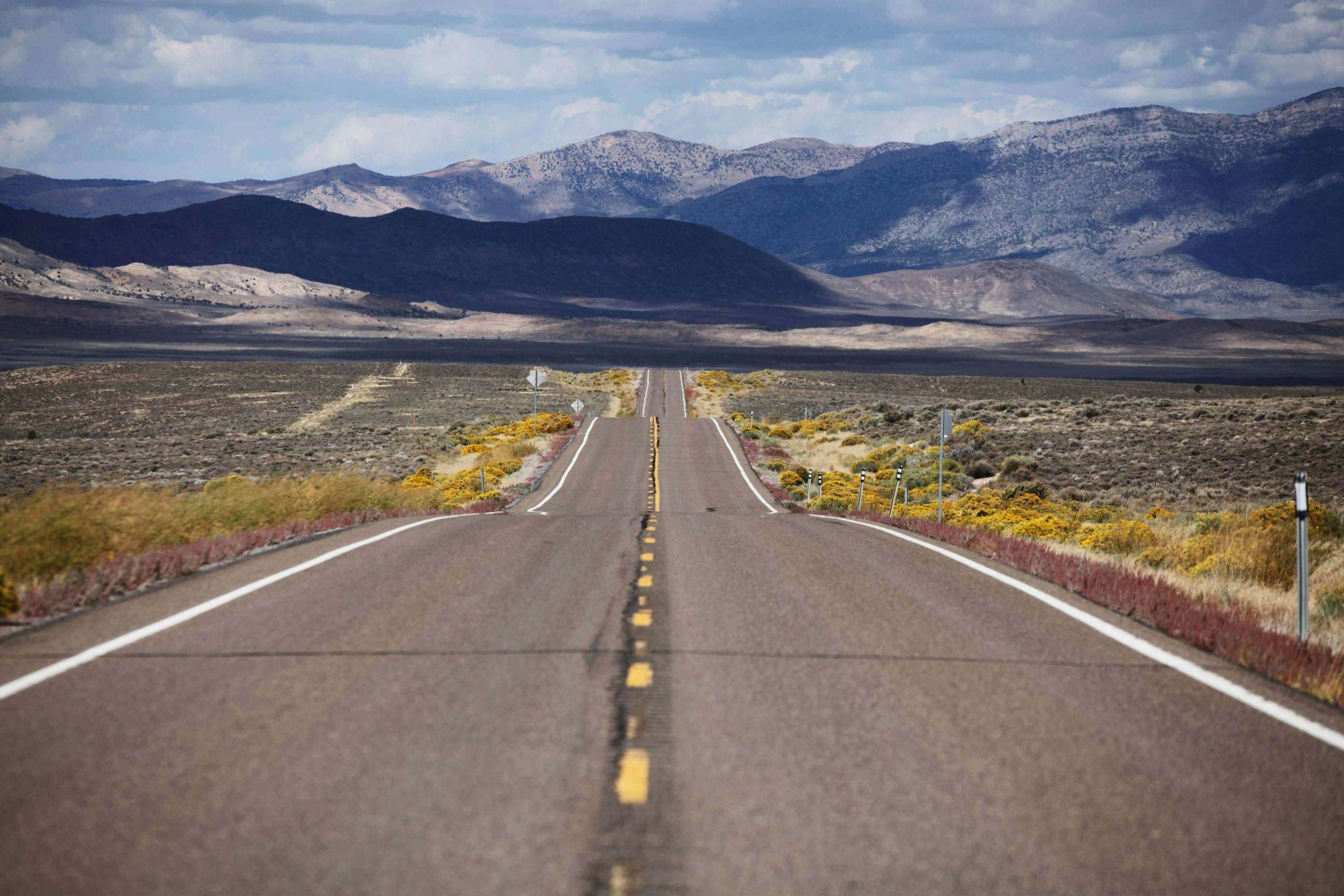 An open road with mountains, hills and vegetation surrounding it. 