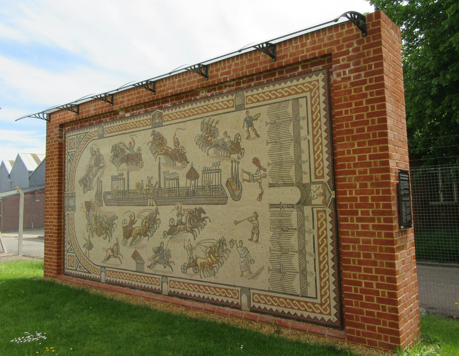 A large mosaic detailing chariot racing on a red brick wall.