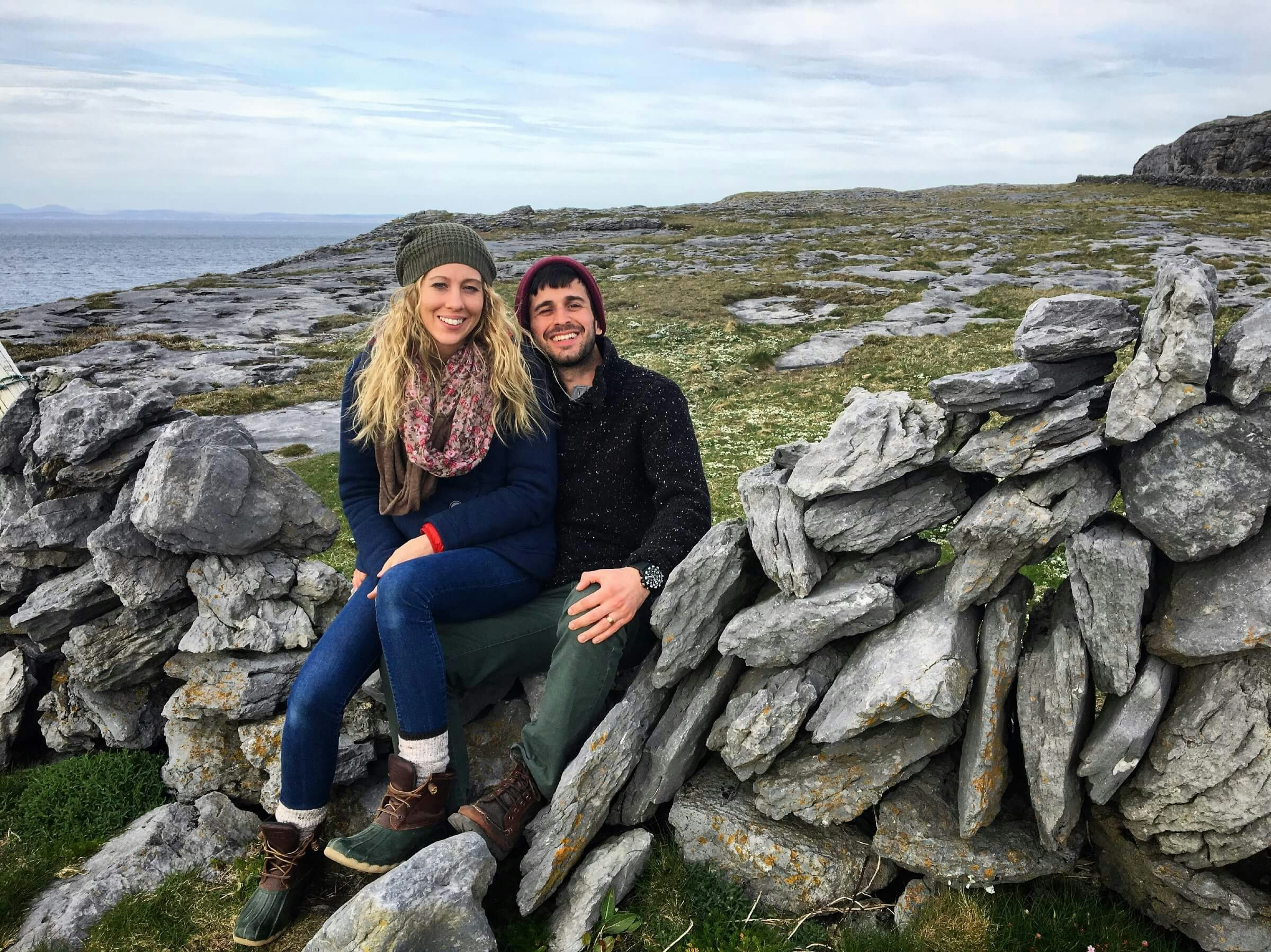 Portrait of smiling man and woman sitting on rocks against cloudy sky in Ireland, Ennis.