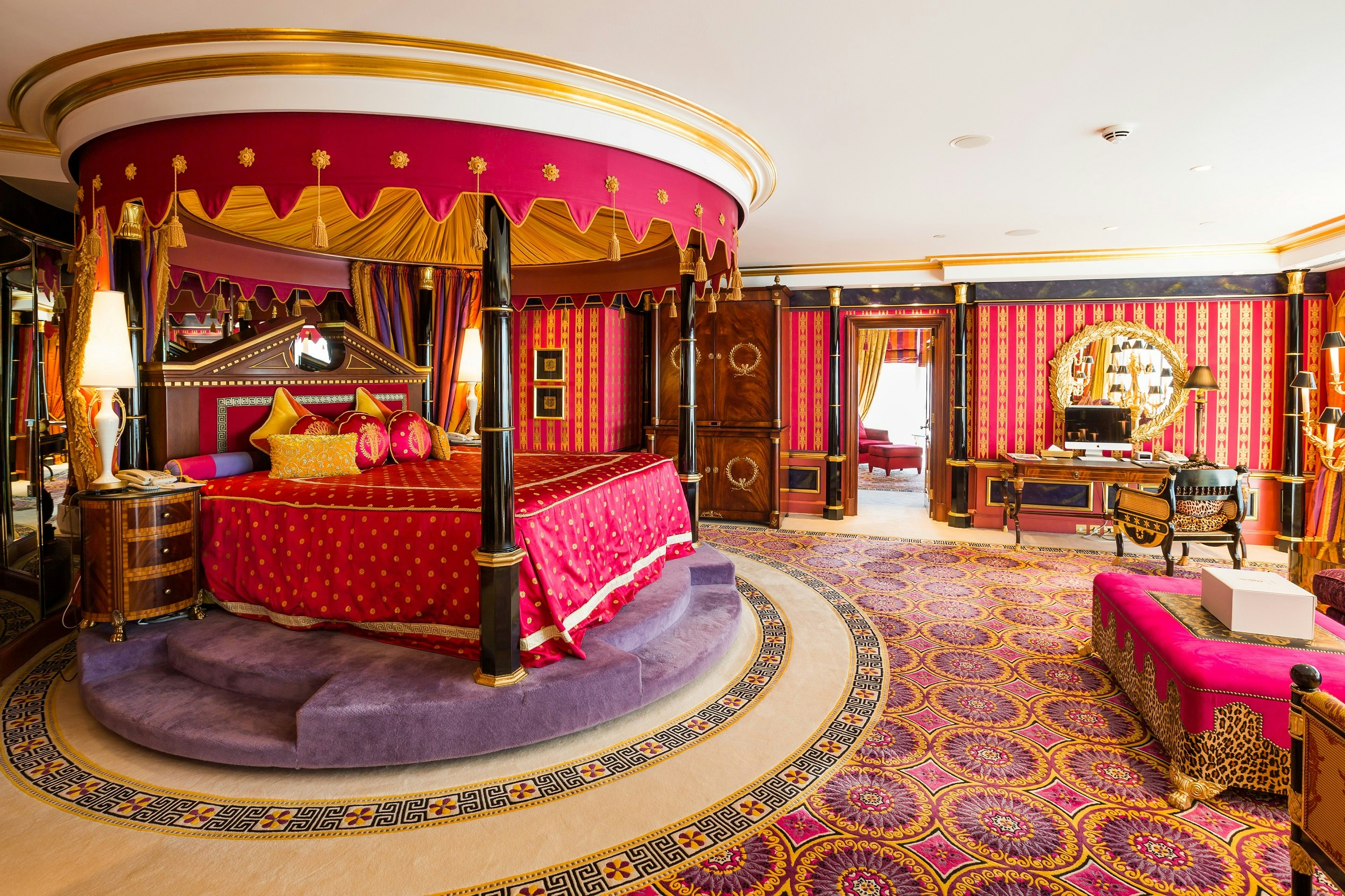 A bedroom with a large canopied bed. The decor is heavily patterned, predominantly in pink, purple and yellow
