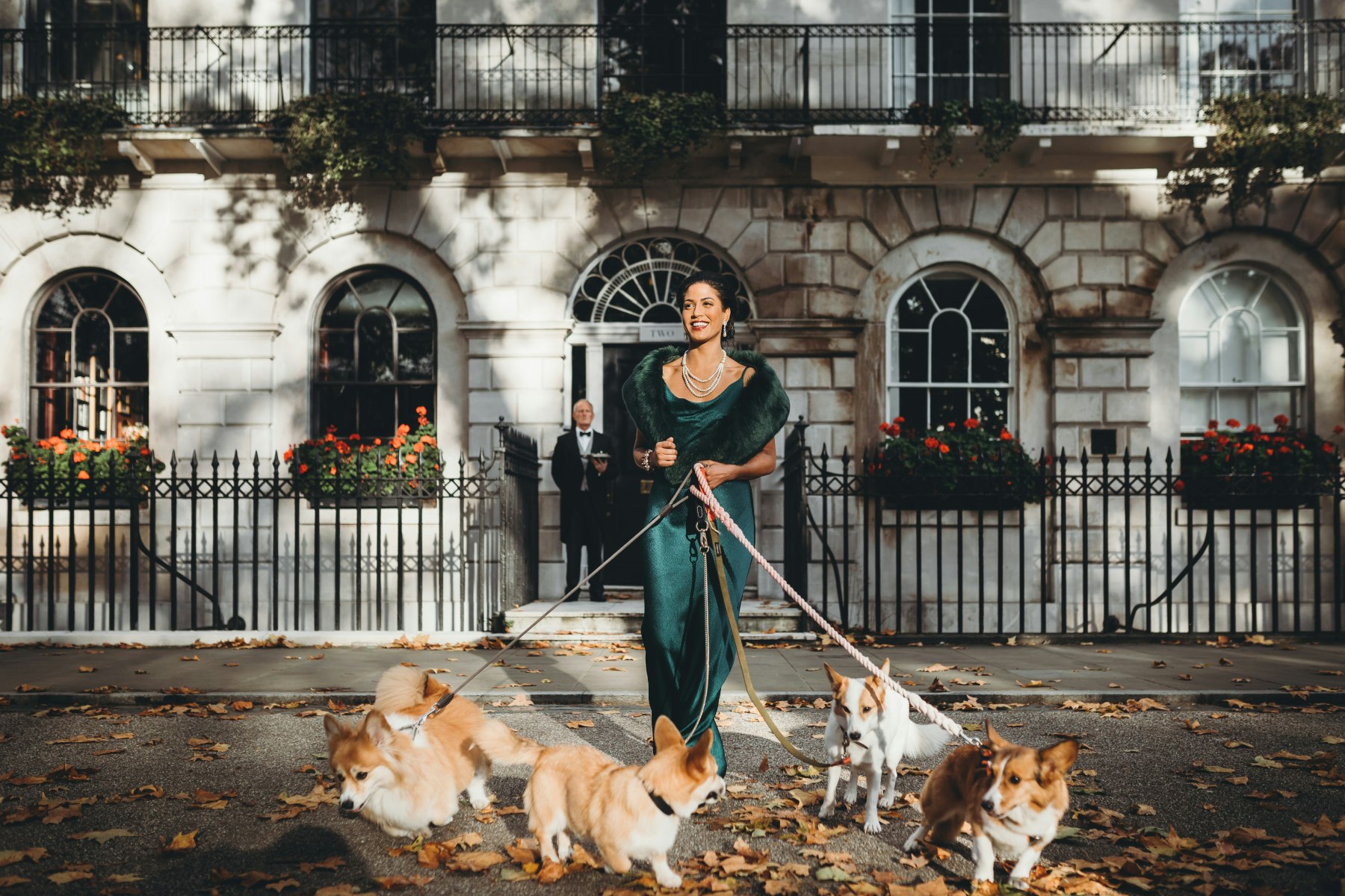 A picture of a Royal Affair guest with a beautiful green gown and four corgis in front of the townhouse