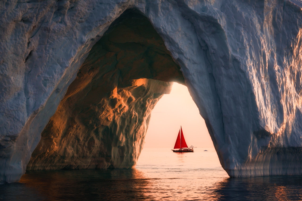 a red sailboat seen through a hole in the ice in greenland