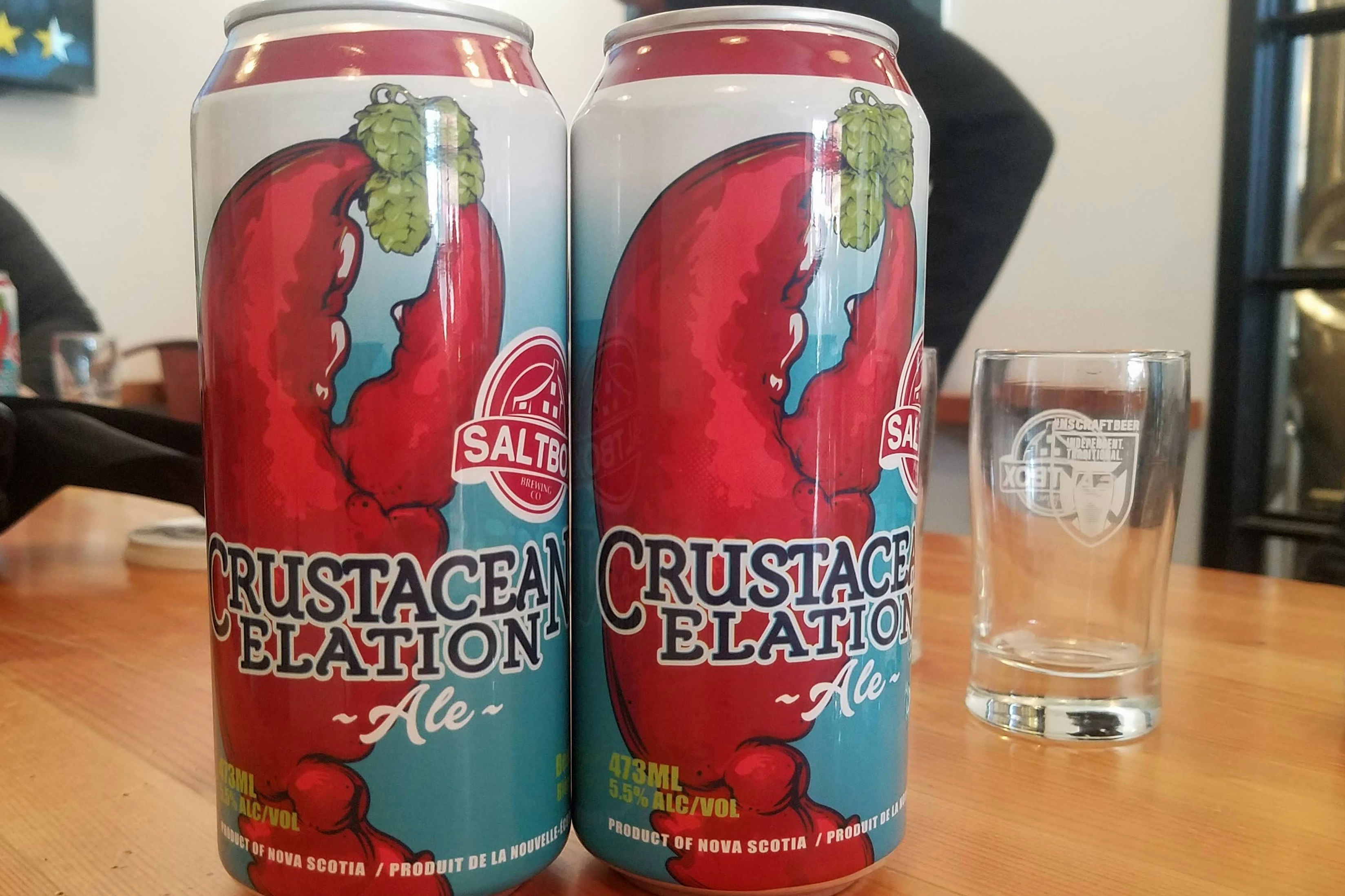 Two large cans of Saltbox Brewery's Crustacean Elation Ale sitting side-by-side on a bar table.