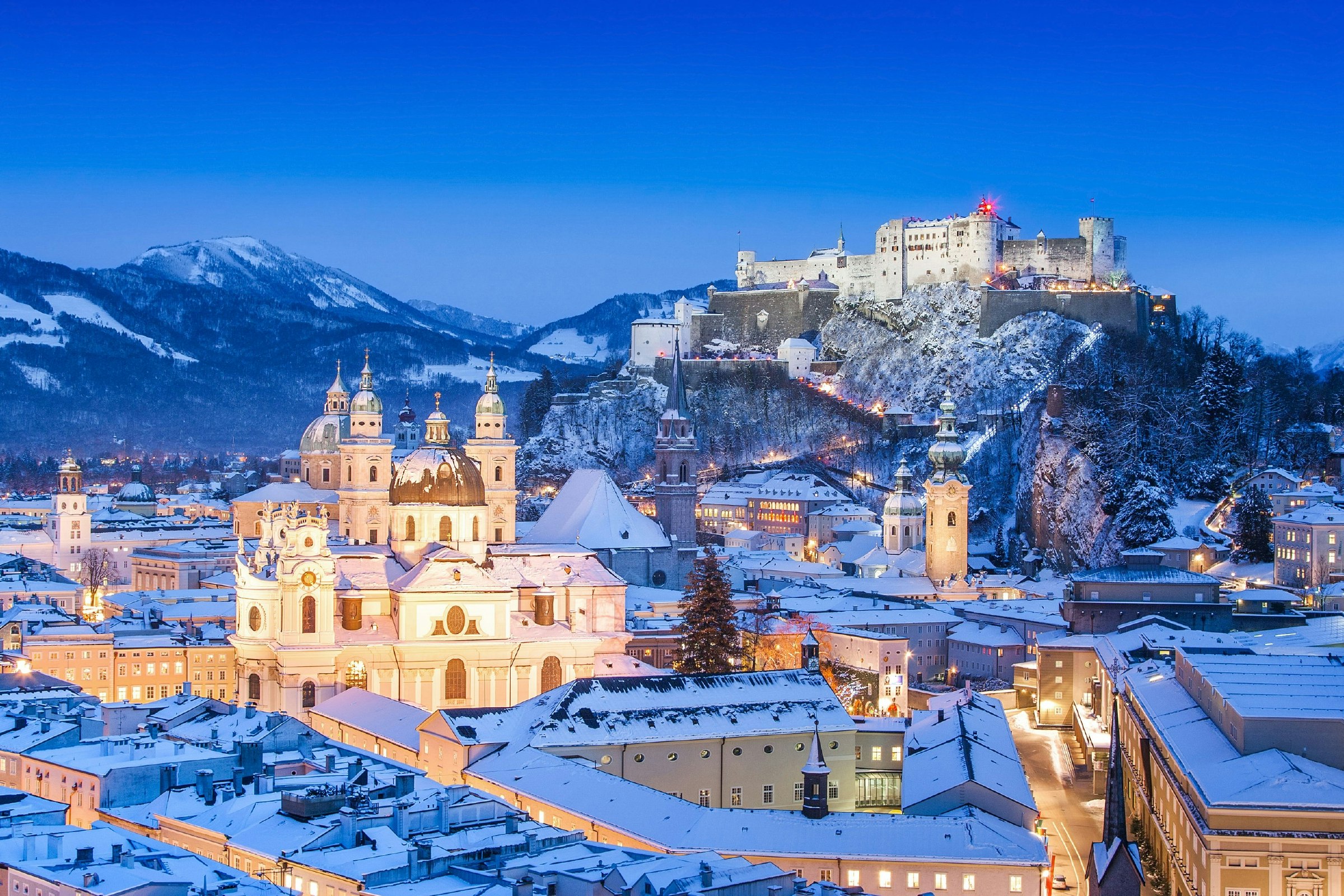 View of the city of Salzburg near dark, with snow-covered Alps in the background.
