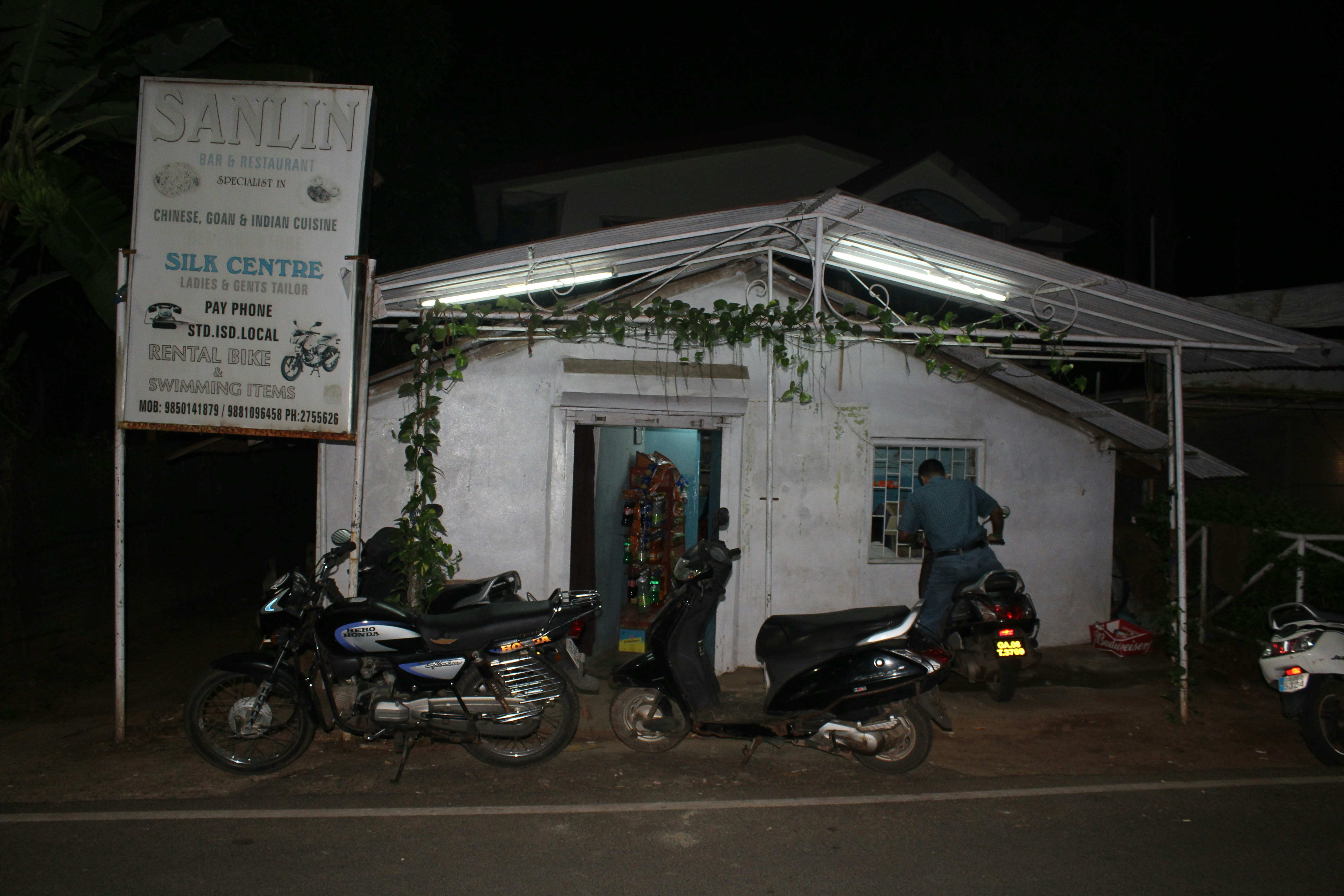The dark exterior of Sanlin Tavern is a simple white concrete building with mopeds parked out front