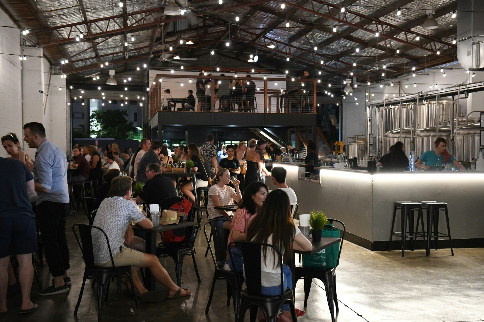 A large, industrial-feeling space with vaulted steel roof is filled with people eating, drinking and socialising.