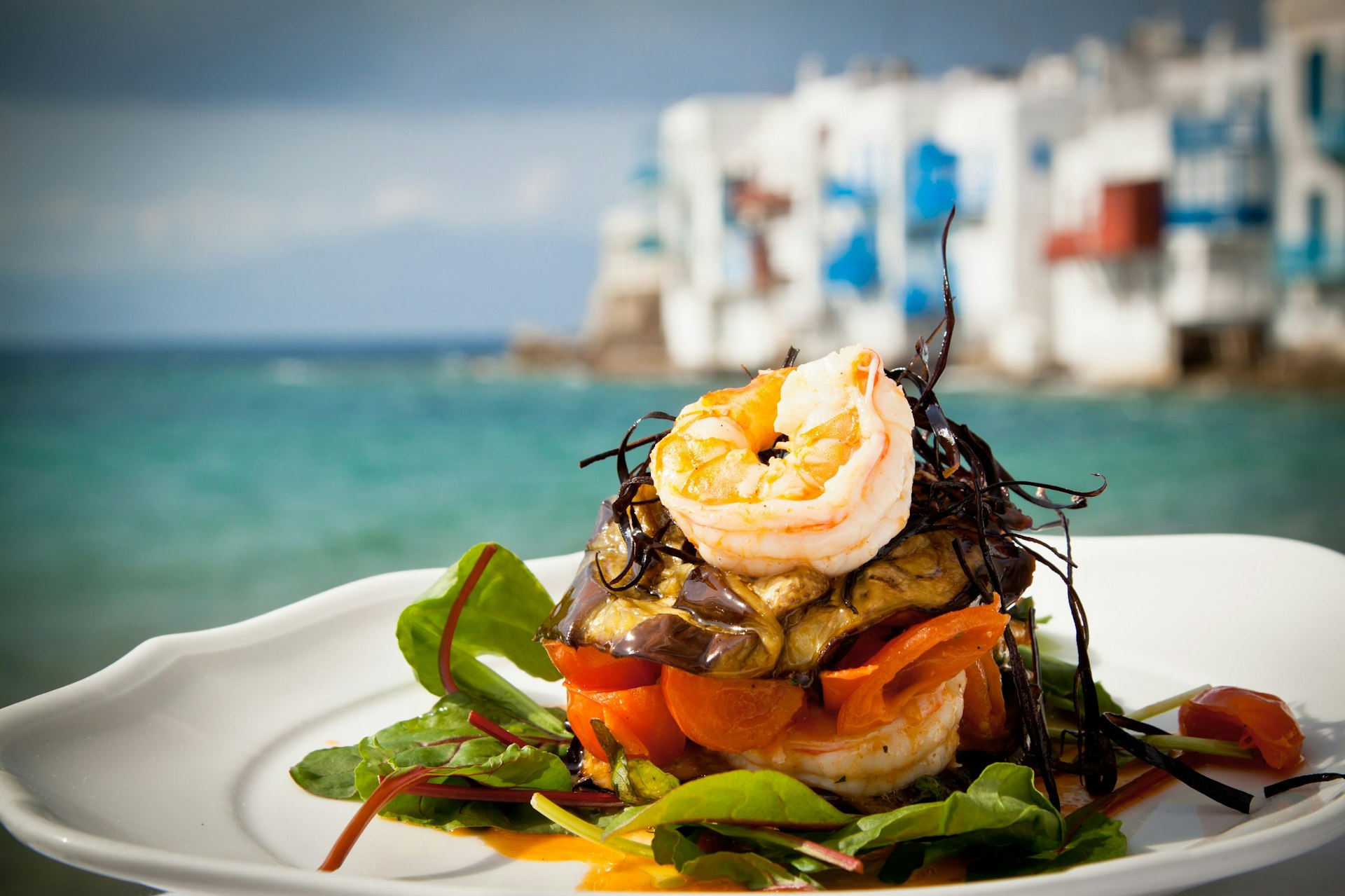 A plate of seafood including prawns on a bed of salad. The sea is turquoise in the background