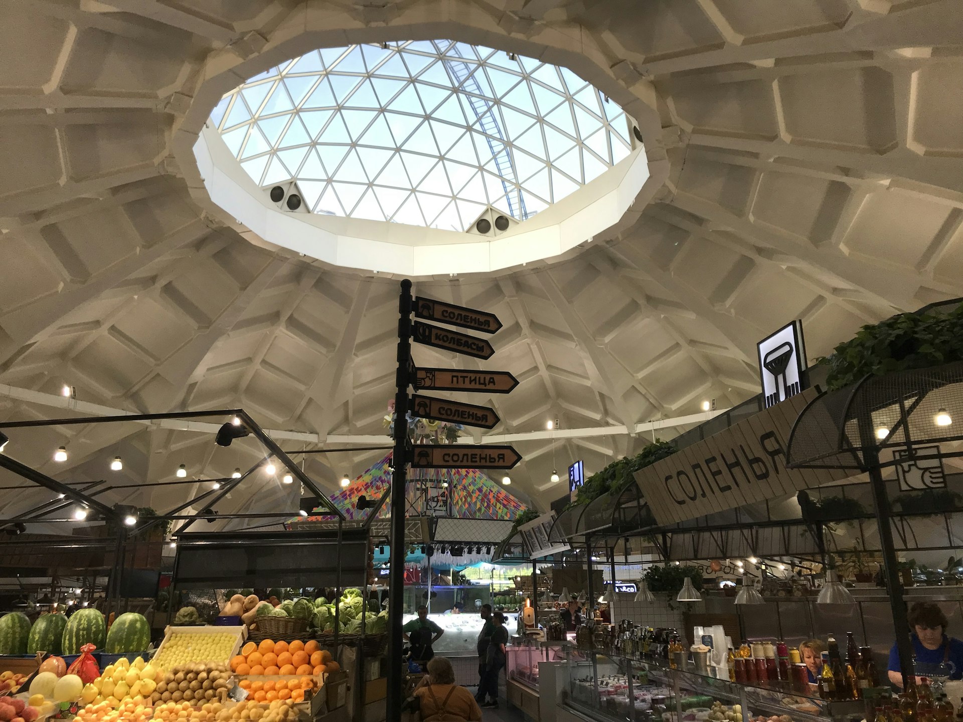 A curved ceiling with a glass domed centre; there is a fruit and veg stall to the left and a row of other market stalls to the right
