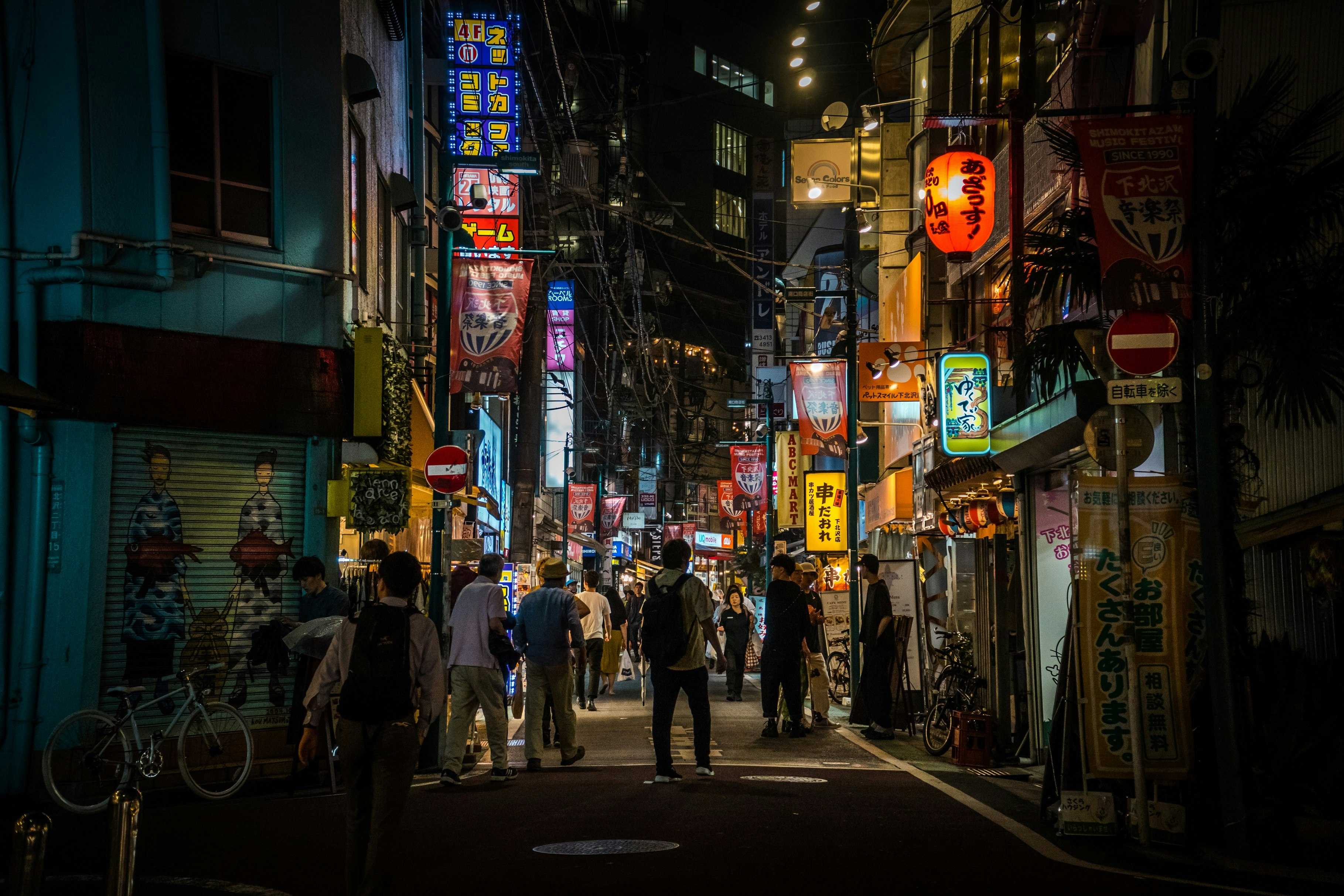 People in the street of Shimo-kitazawa district. It is evening and the various neon lights illuminate the scene.
