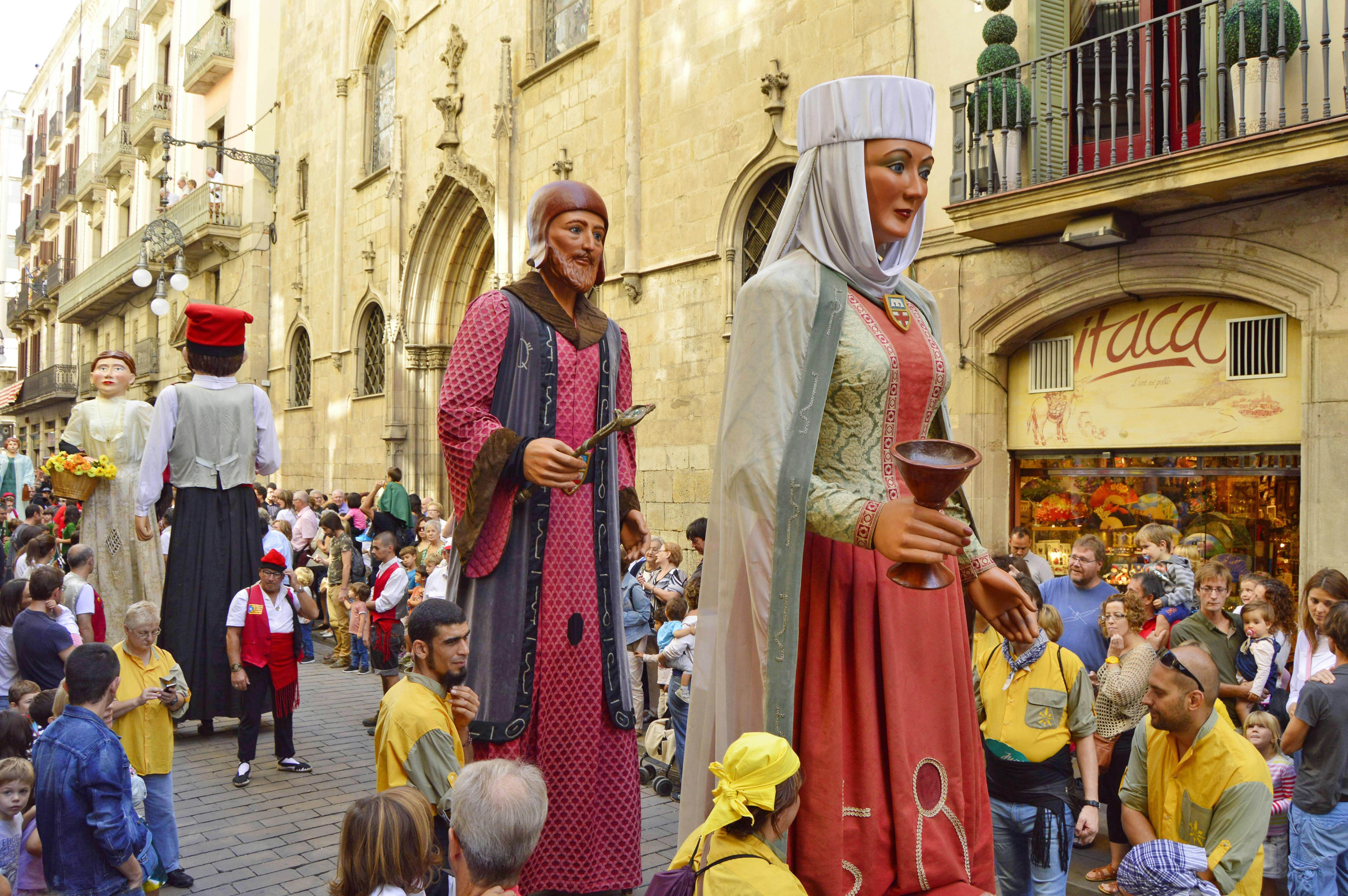 Colourful giants parading through La Rambla during La Mercè festival; the giants are made from papier-mâché and wear traditional religious dress, while onlookers watch the procession.