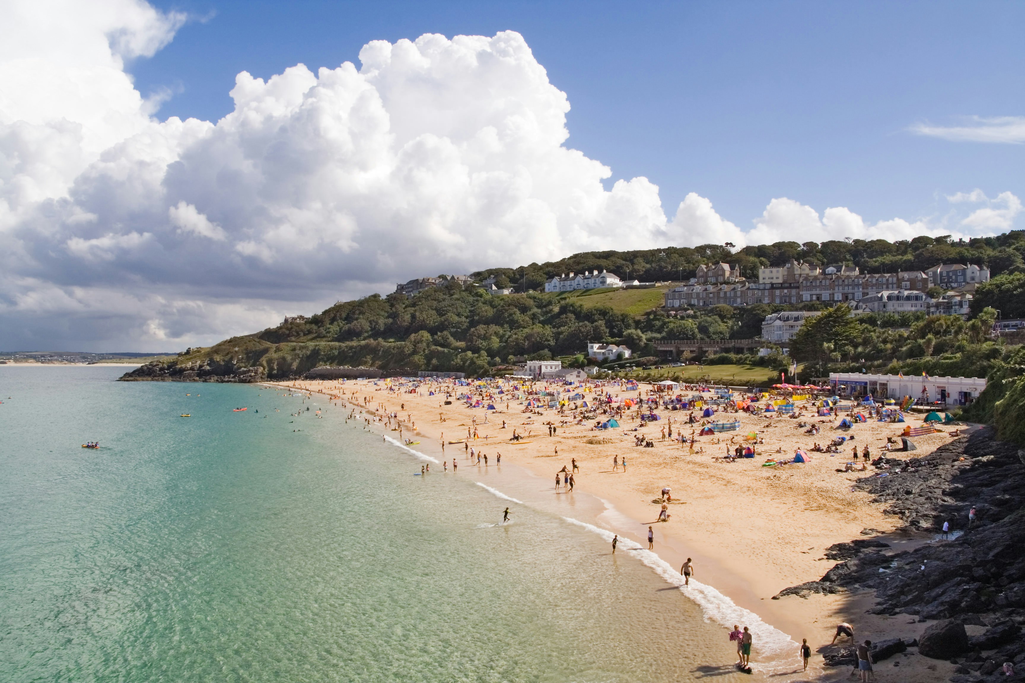 An aerial view of Porthminster beach in St Ives, Cornwall. The turquoise waters lap against the bright white sand, which is busy with sun seekers.