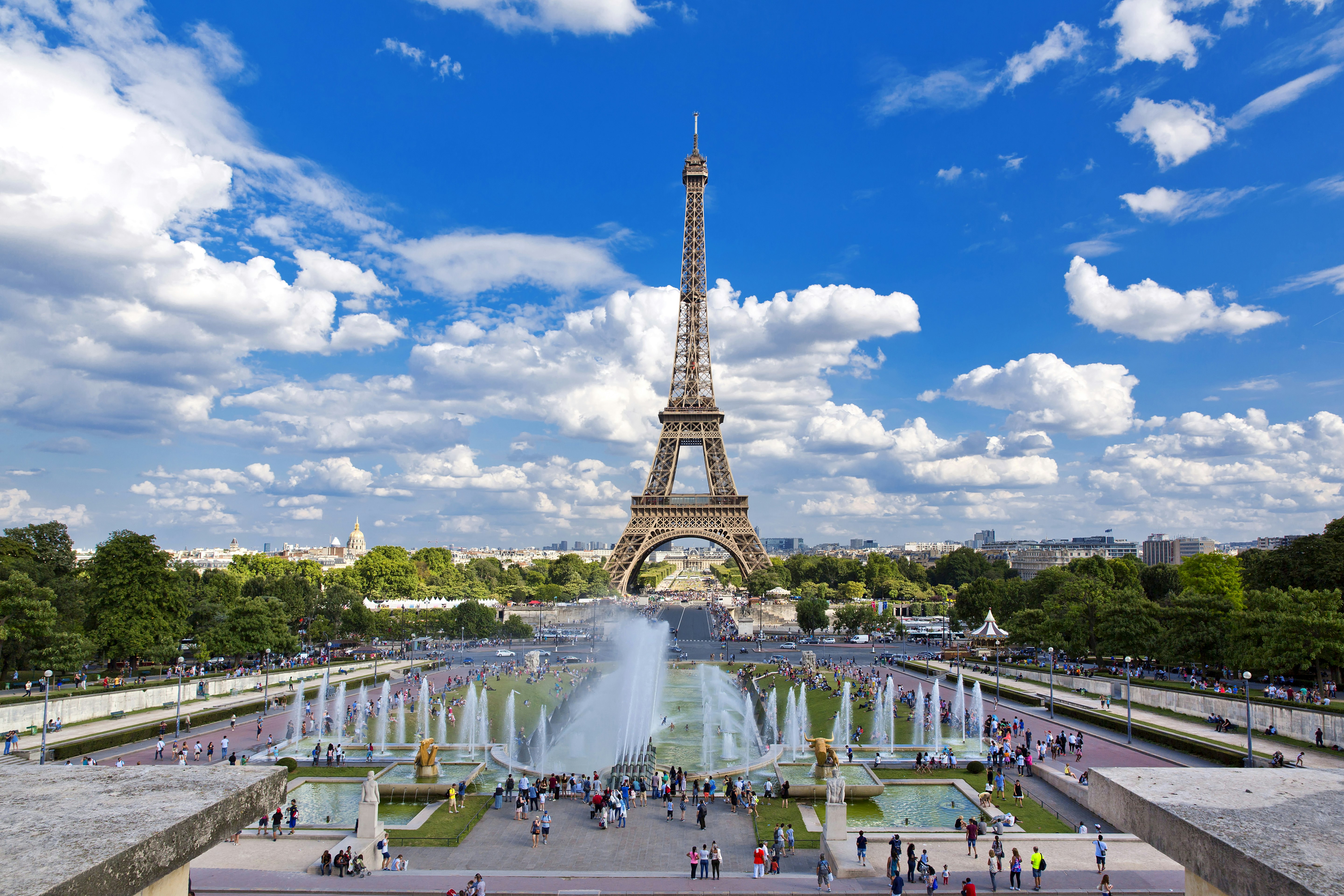 Eiffeltornet fångat en ljus, solig dag från Trocadéro Gardens på andra sidan floden.  Många besökare är samlade i trädgårdarna.