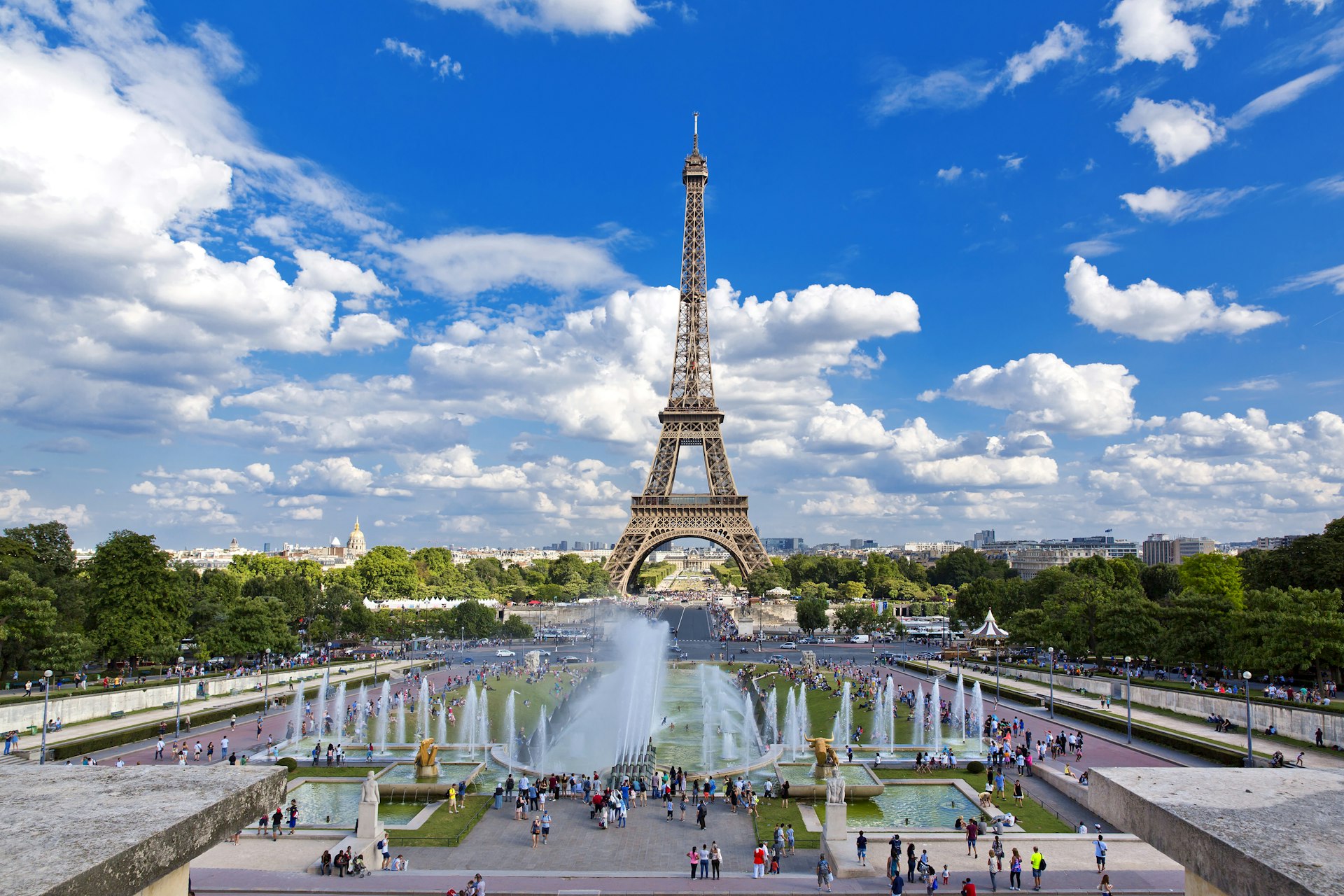 The Eiffel Tower captured on a bright, sunny day from the Trocadéro Gardens across the river. Many visitors are gathered in the gardens.