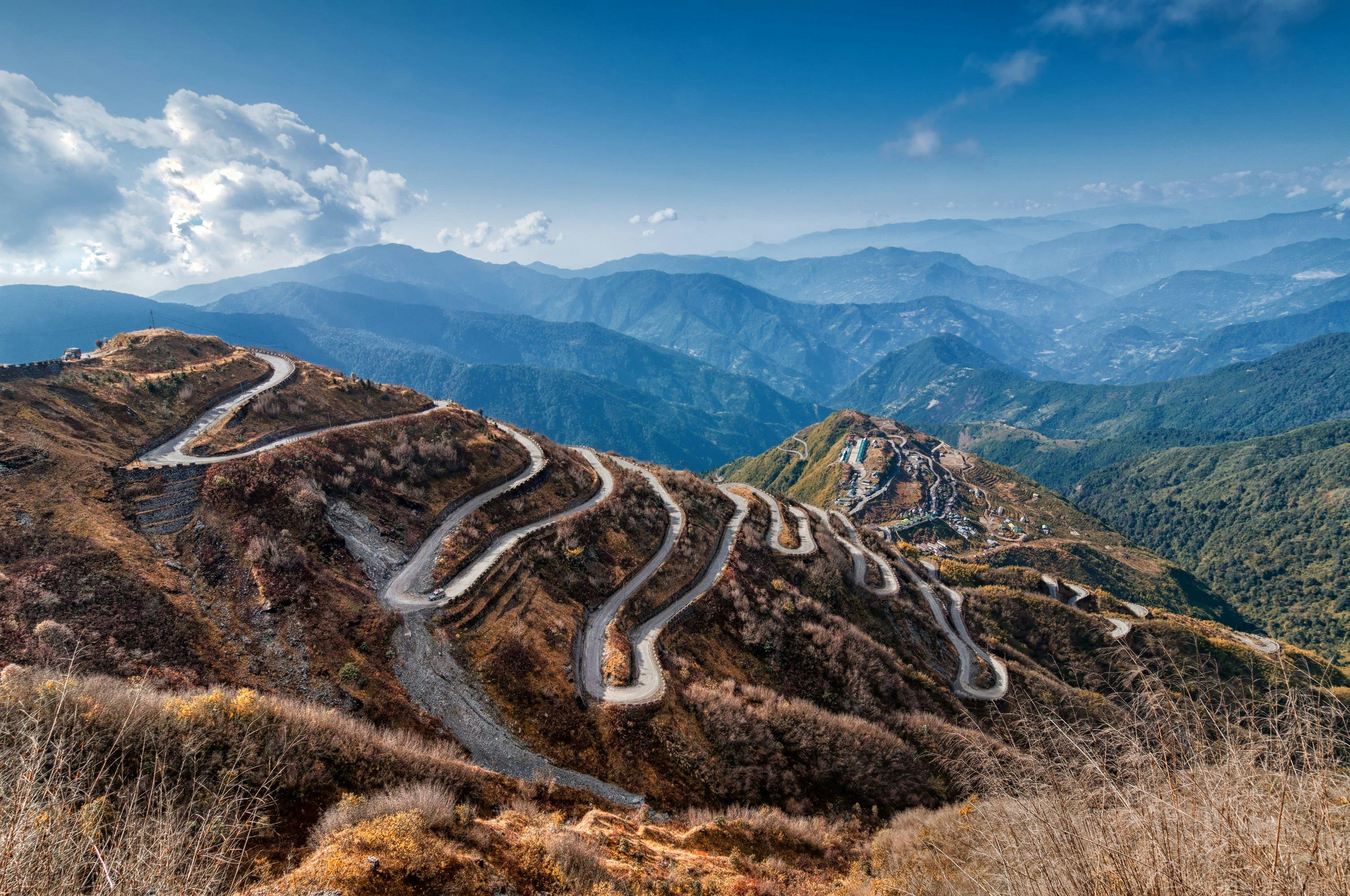 A single road winds its way up a steep mountain in Sikkim. With more mountains visible in the distance.