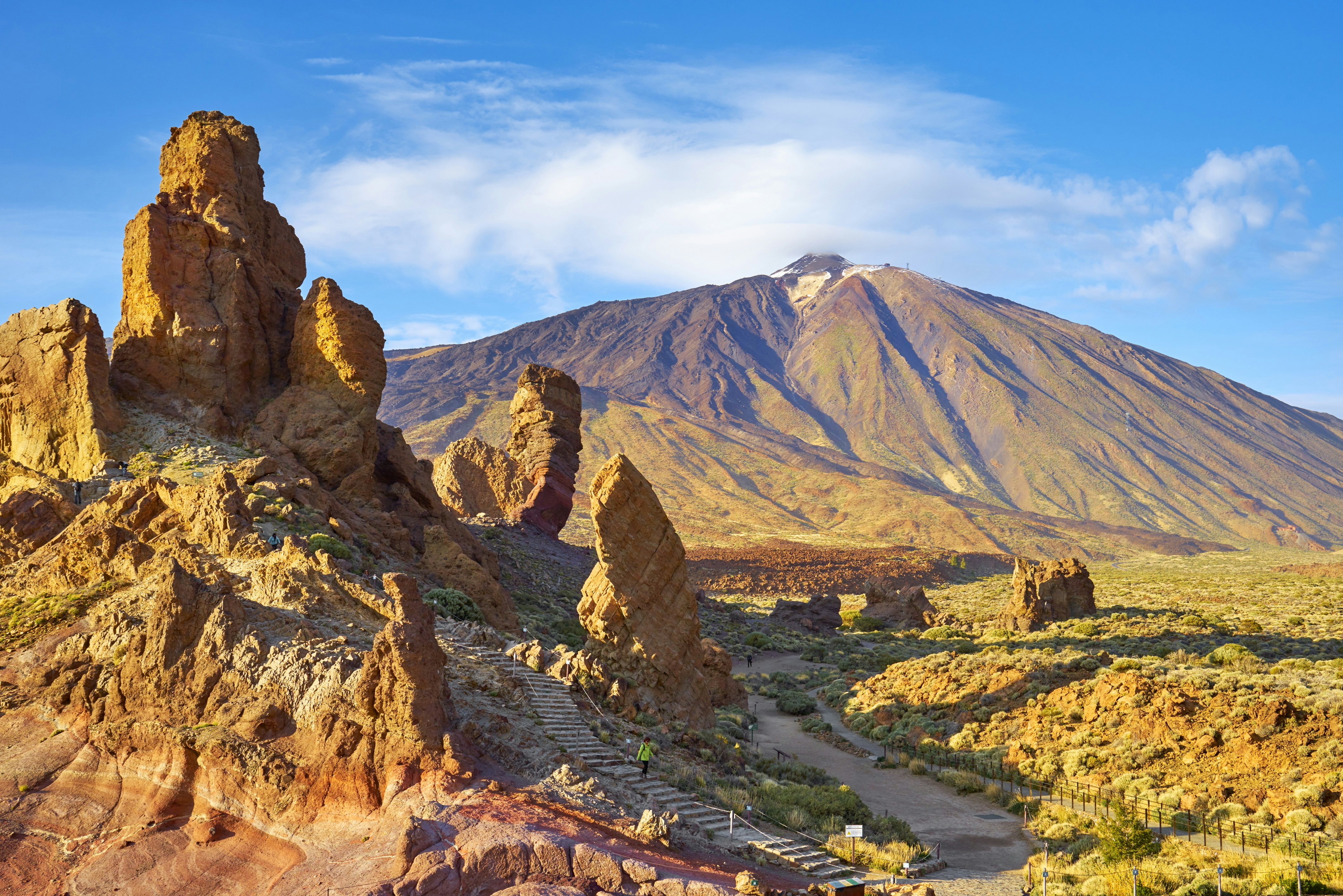 Sand-colored rock formations jut into the sky with the volcanic cone of El Teide in the background at Teide National Park, Tenerife