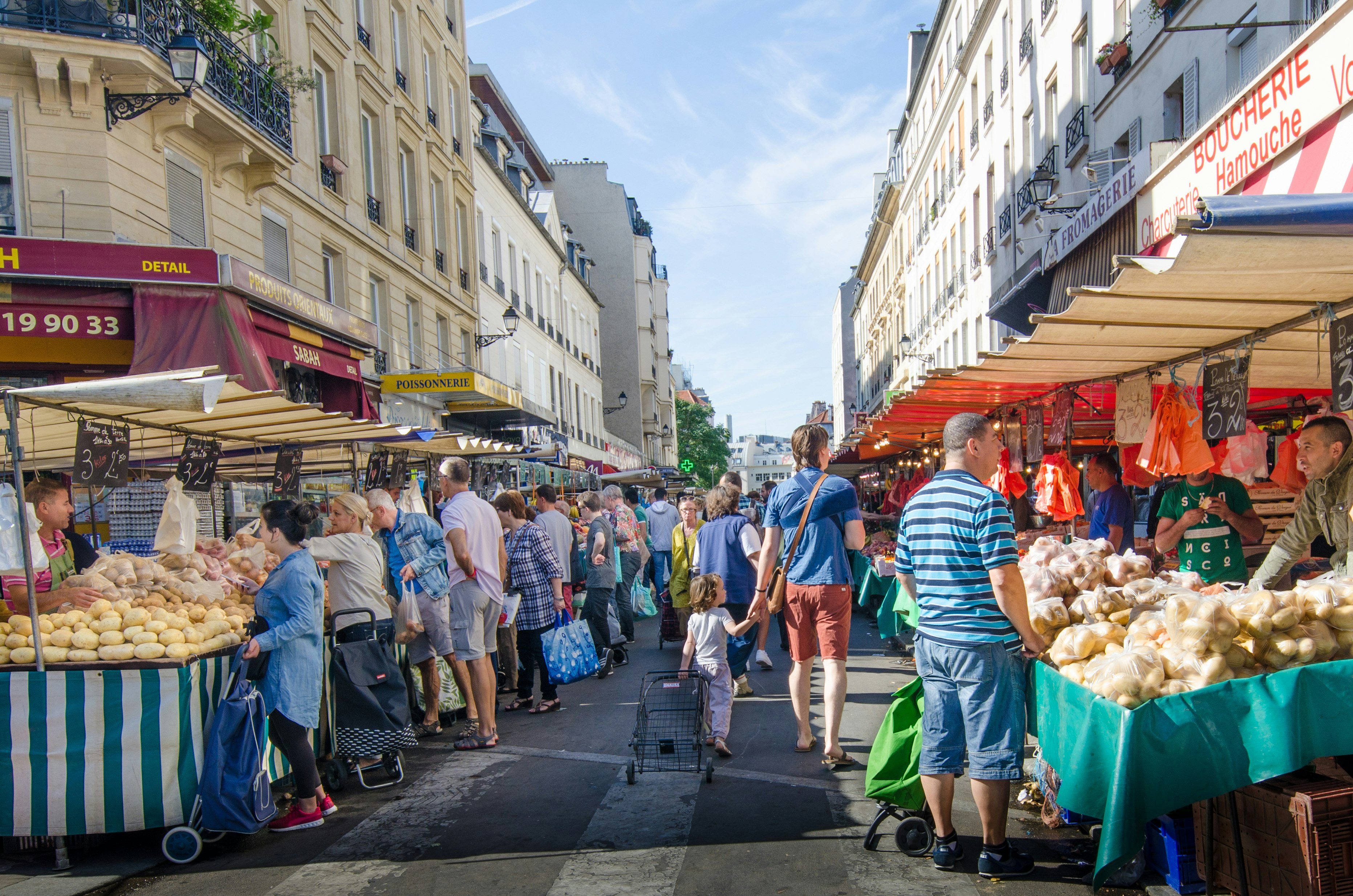 Crowds of people browse the stalls of Marché Bastille in Paris. The market stalls run down either side of a long avenue.