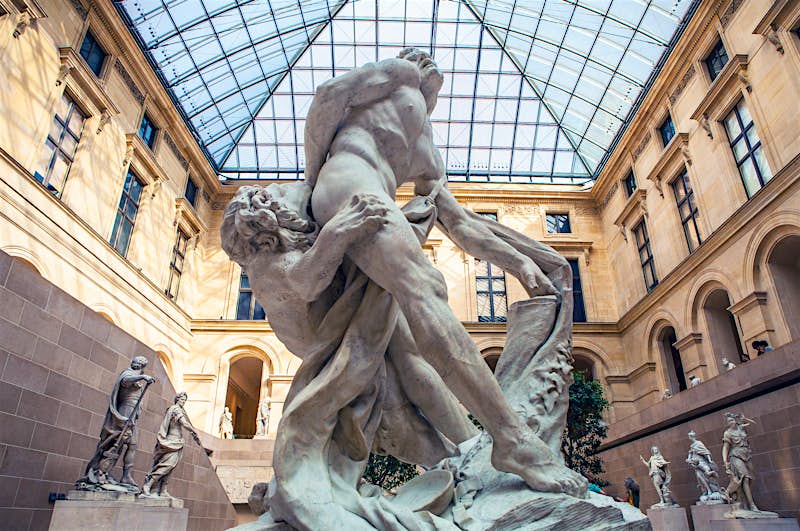 Louvre_Museum_Paris_Lonely_Planet.jpg Sculpture hall of the Louvre museum, Paris, with the image focusing on the Milo of Croton statue: a man with his hand stuck in a tree being devoured by a lion
