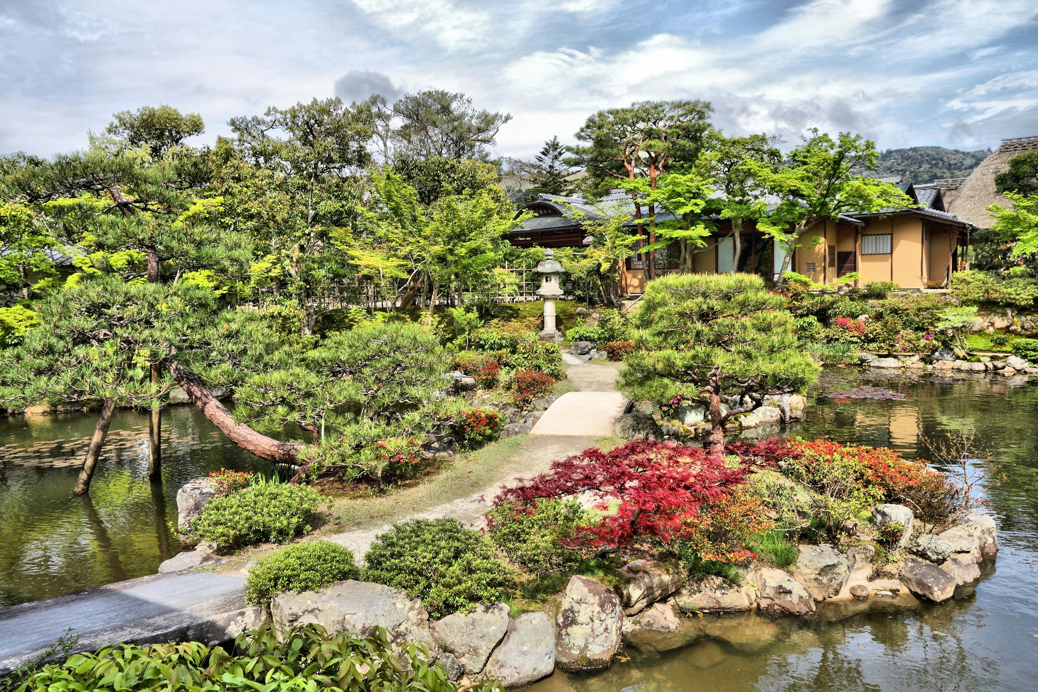 The elegant Isui-en garden, with a path winding past lakes, stones, trees and shrubs to a low-level building beyond.