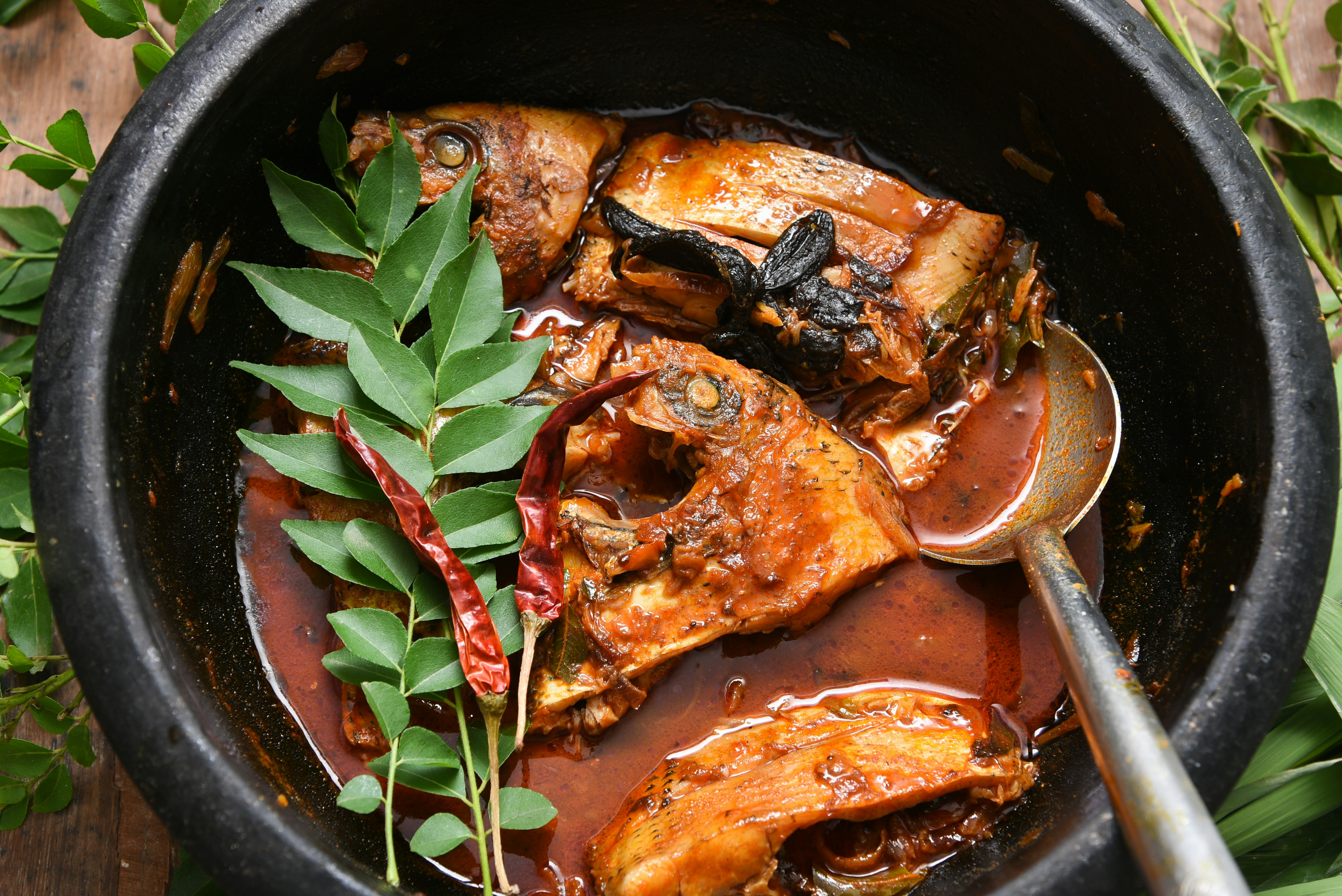 A close-up of fish curry, with chillies and spices, in a large black bowl