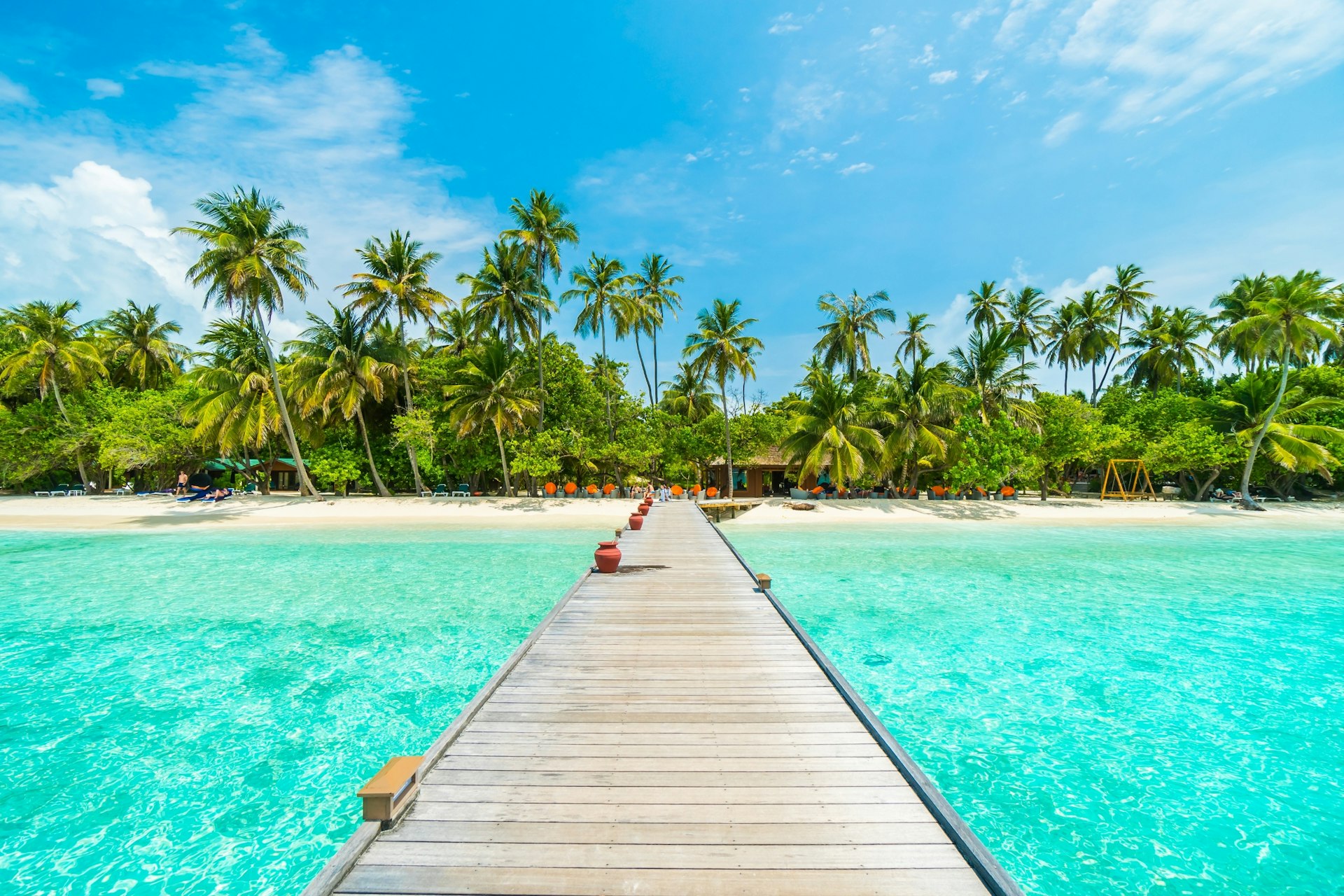 A wooden walkway extends across the sea to a beach in the Maldives