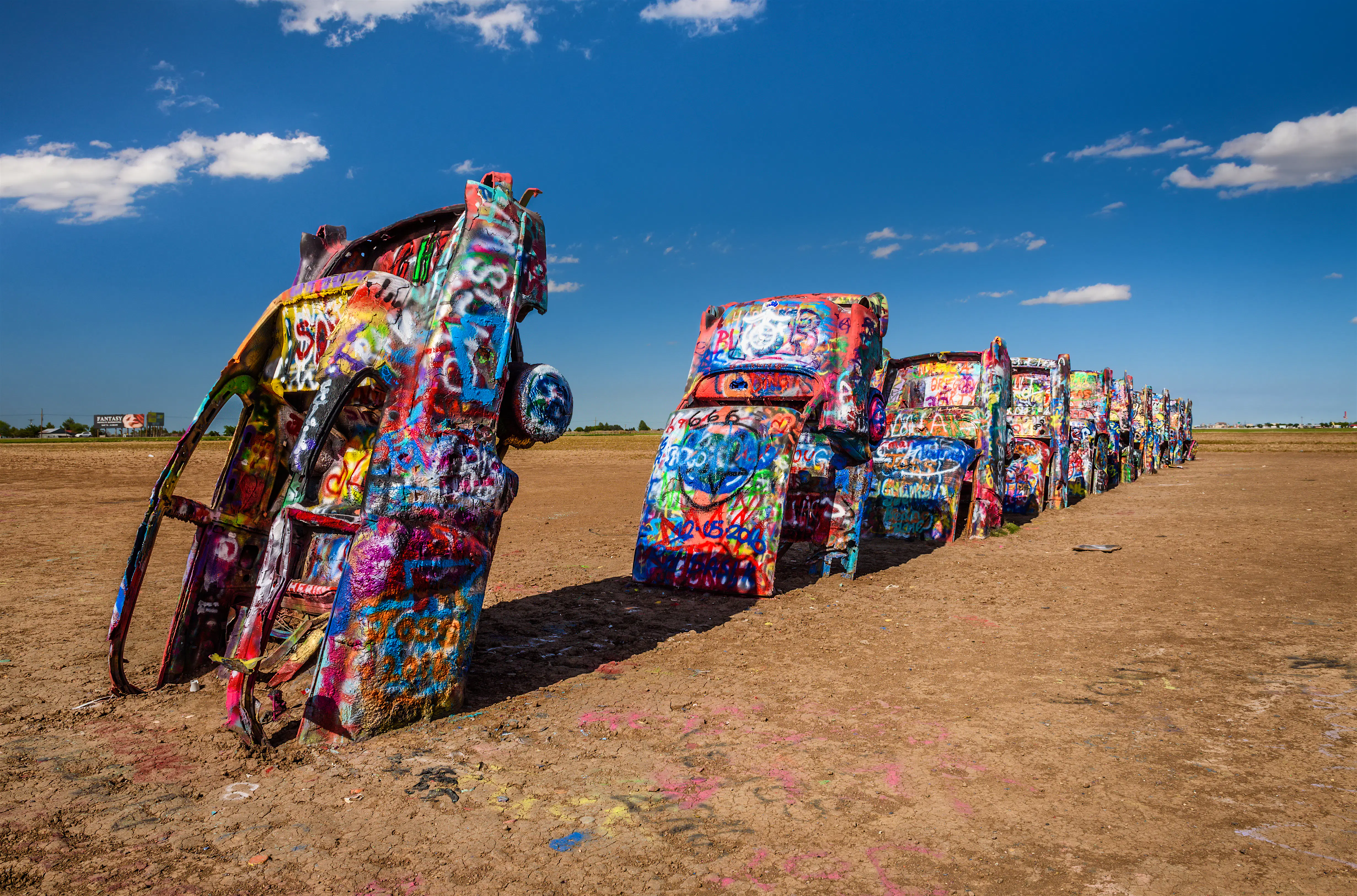 shutterstockRF_449728684 (1).jpg A row of 10 Cadillacs with their hoods buried in the earth stretches out. Each one is covered in colorful marks and graffiti