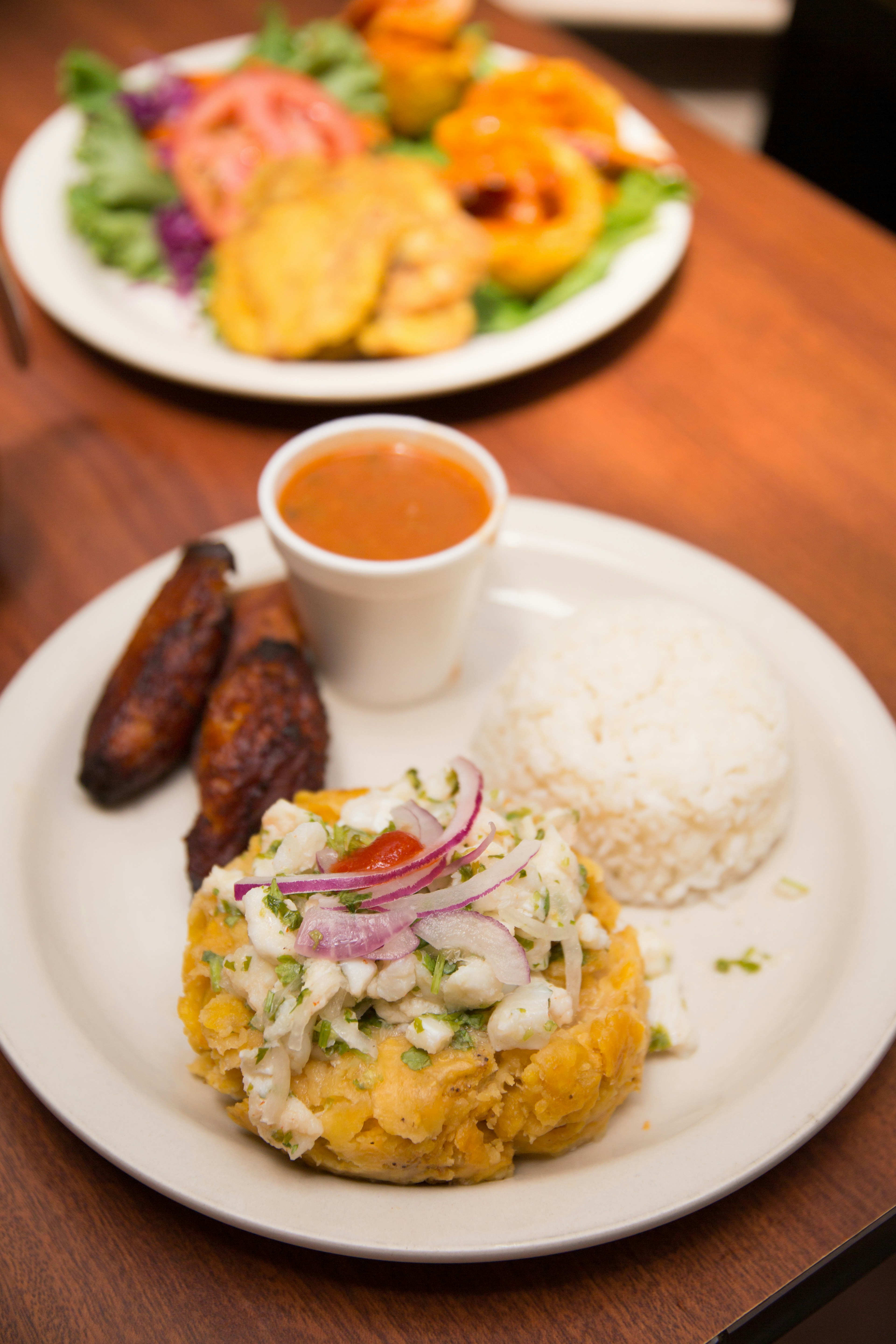 A white plate loaded with mofongo, a fried plantain dish, accompanied by rice and relish