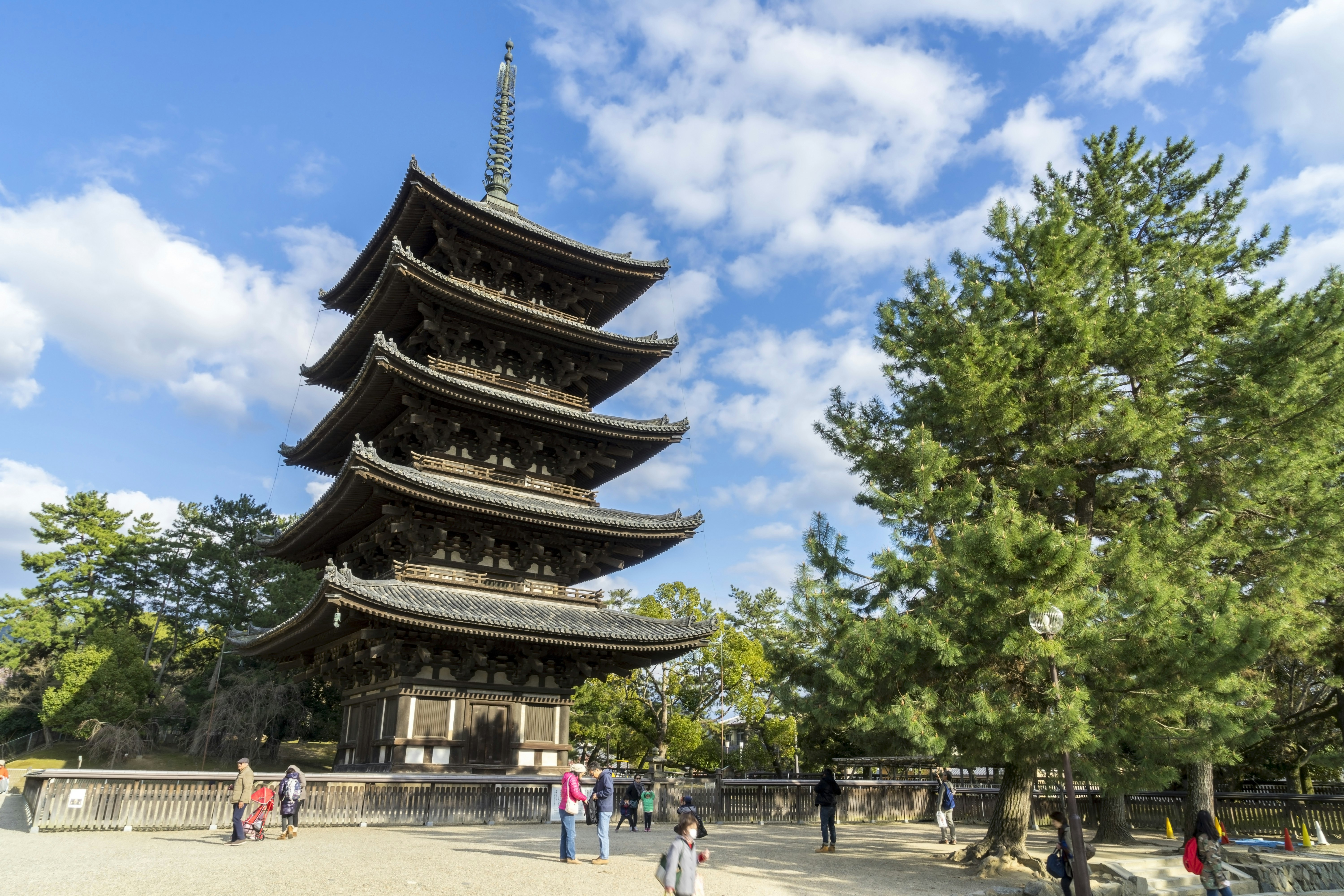 En femvånings pagod vid Kōfuku-ji-templet i Nara sträcker sig mot himlen;  det finns människor utanför den och träd bredvid den. 