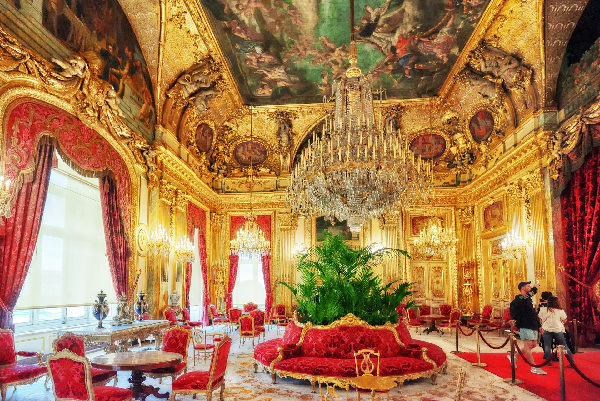 One of the grand rooms of the Napoléon III apartments; lavish chandeliers dangle from the ceiling, red-tasselled curtains hang around the windows and the ceiling is gilded with gold.