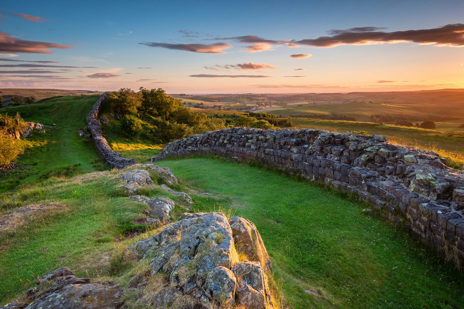 Hadrian's Wall as the sun sets creating an orange glow in the distant clouds