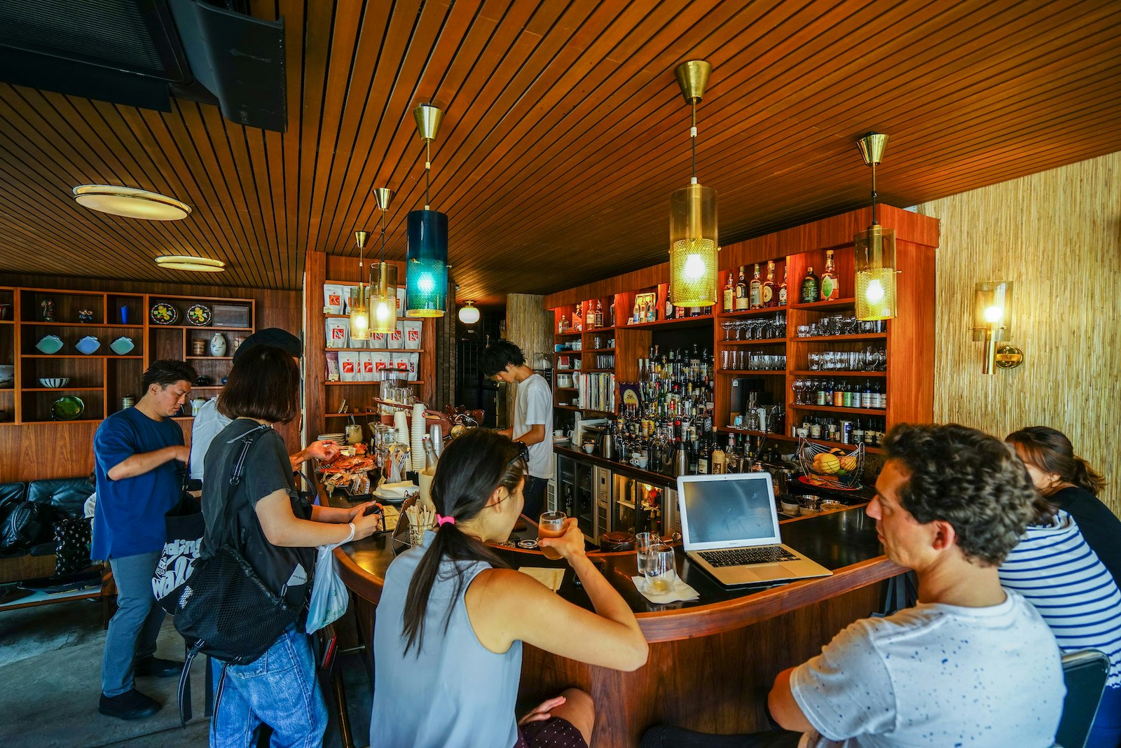 Small group of people in a Tokyo espresso and cocktail bar; one man has a laptop on the bar